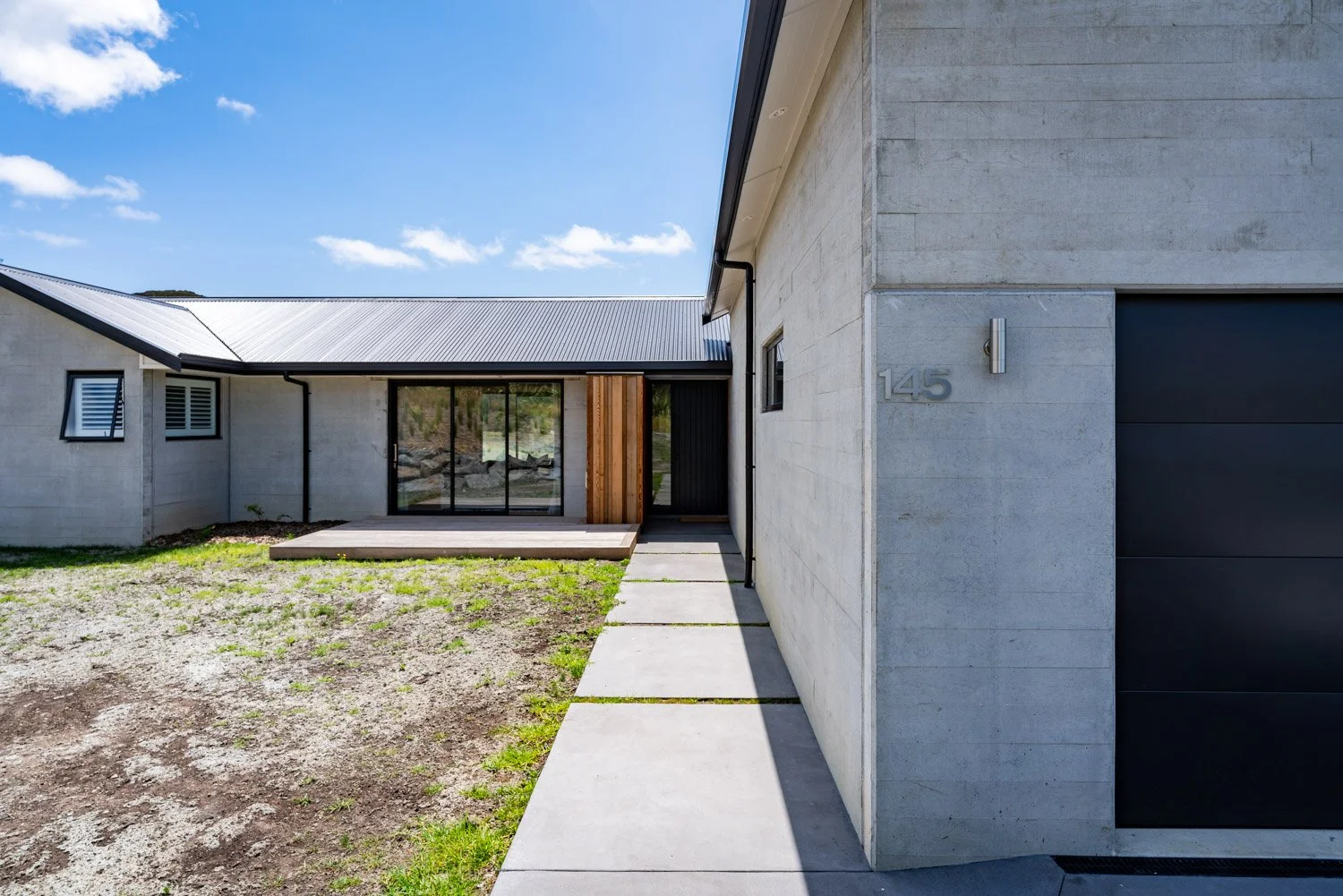 Custom Modern home with concrete walls, black garage door, and wooden accents, under a blue sky with a few clouds.
