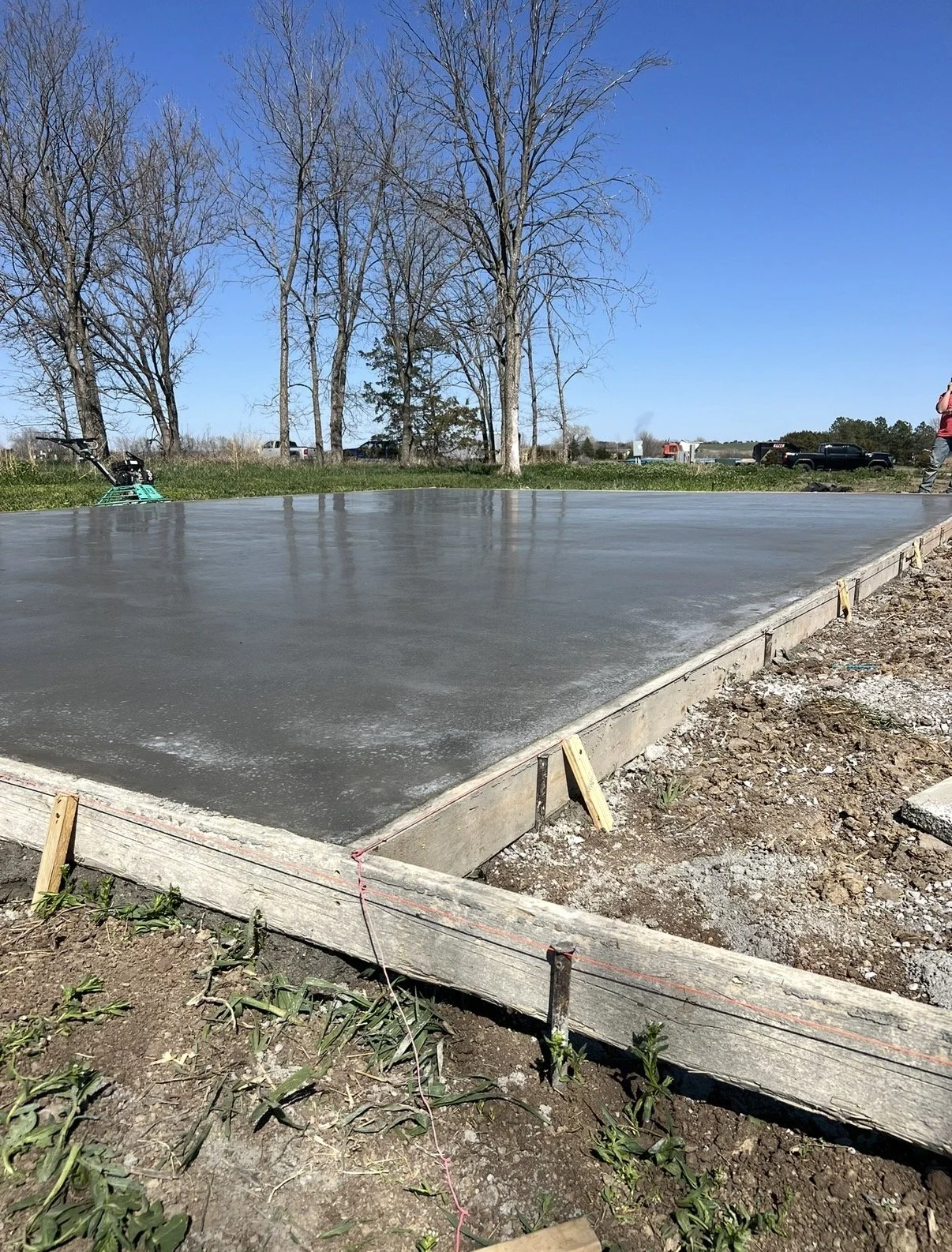 Concrete slab curing on a construction site with trees and parked vehicles in the background.