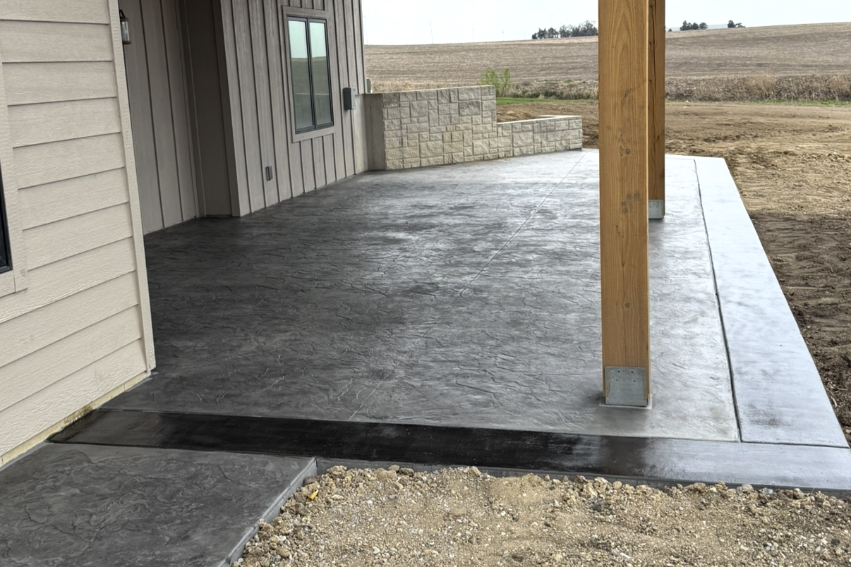 Photo of a newly constructed house patio with concrete flooring, a wooden post, and a view of an open field in the background.