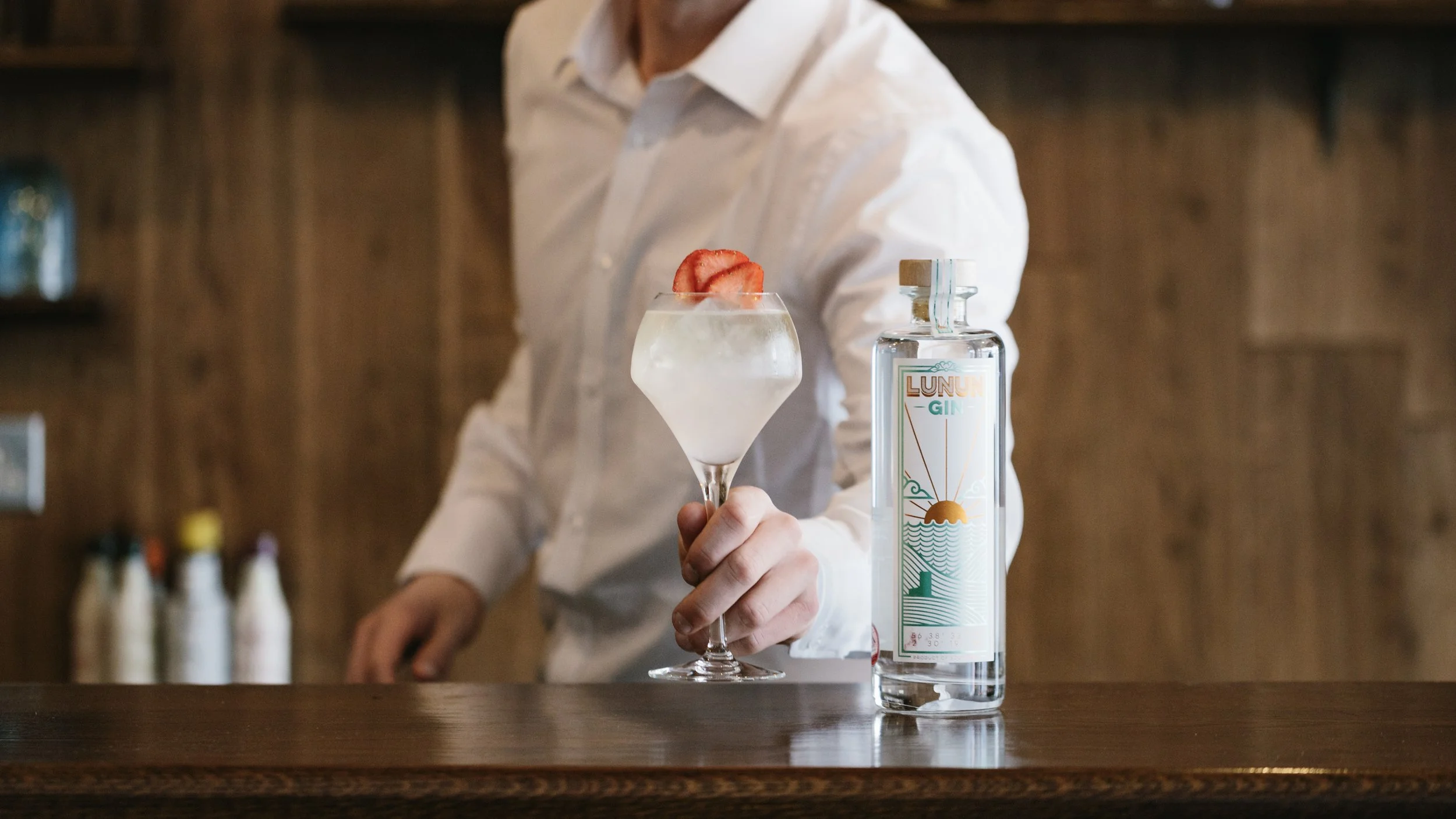 cocktail being served on a bar with a bottle of Lunun Gin