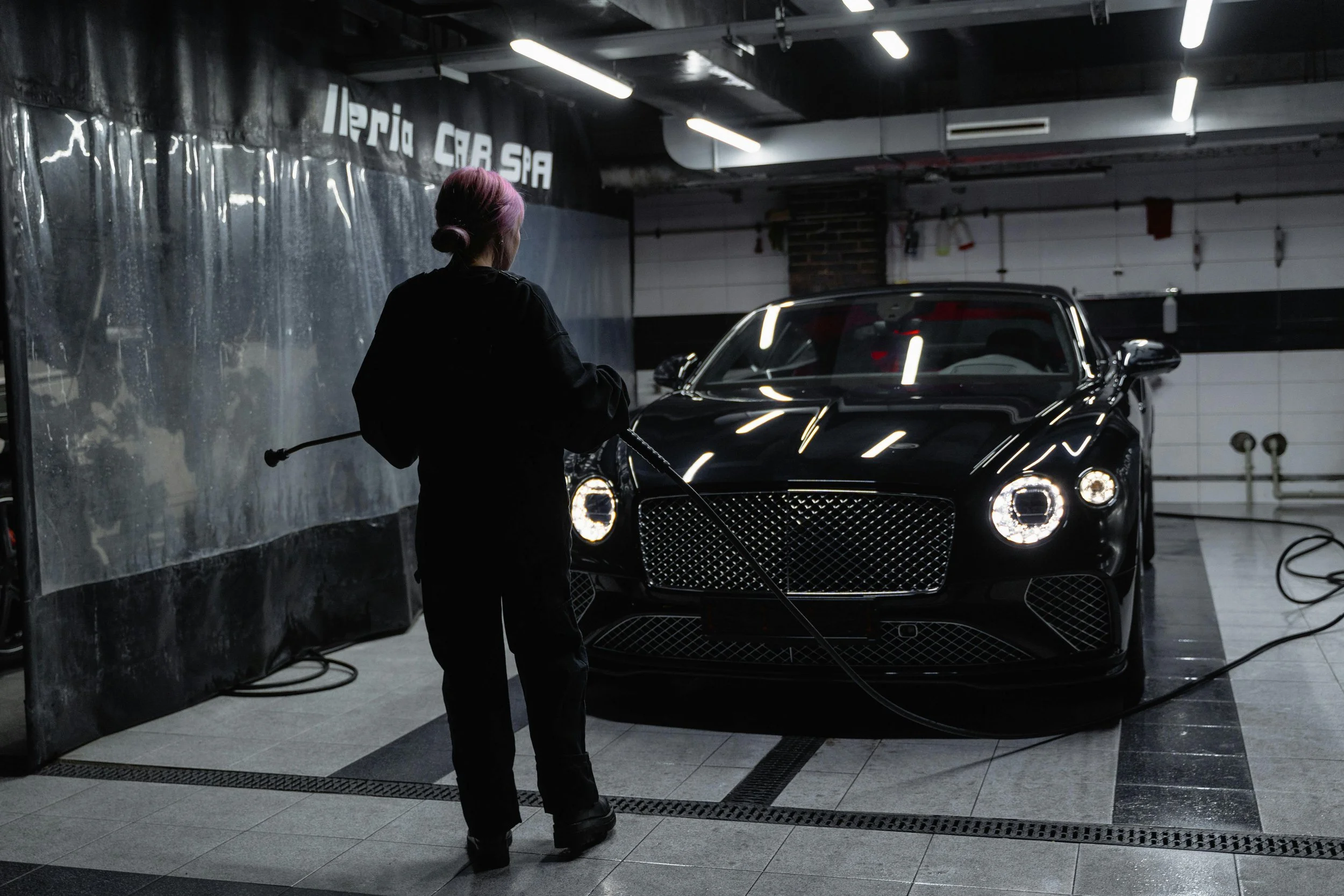 Person washing a sleek black luxury car in a garage or car wash bay.