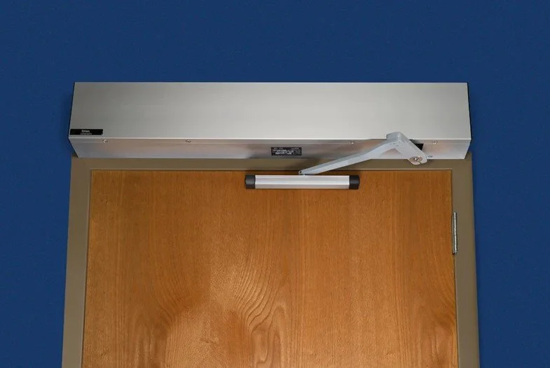 View of a door with a mounted automatic door closer and a safety sensor.