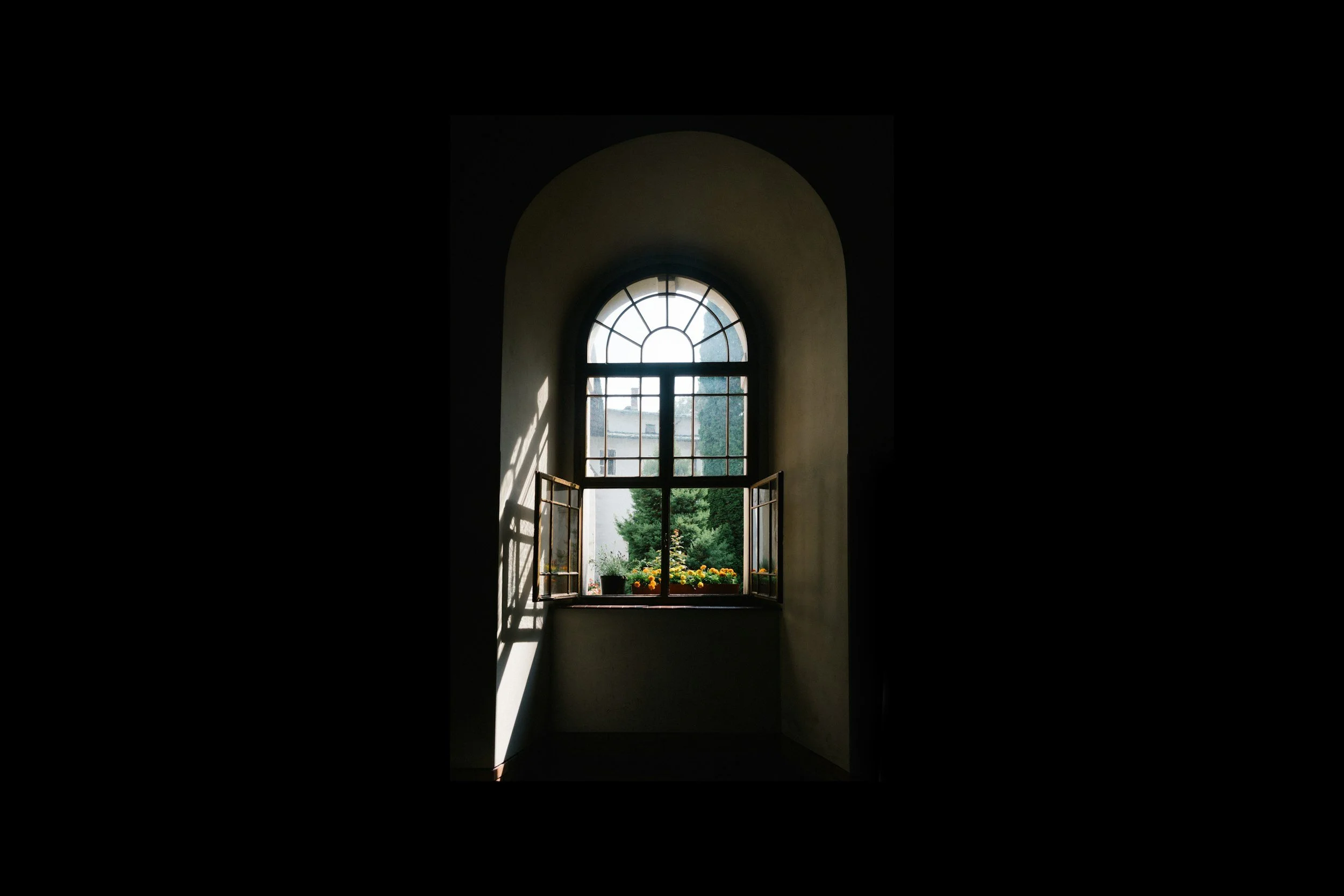 Looking through an open window, a garden with potted plants and trees is visible outside.