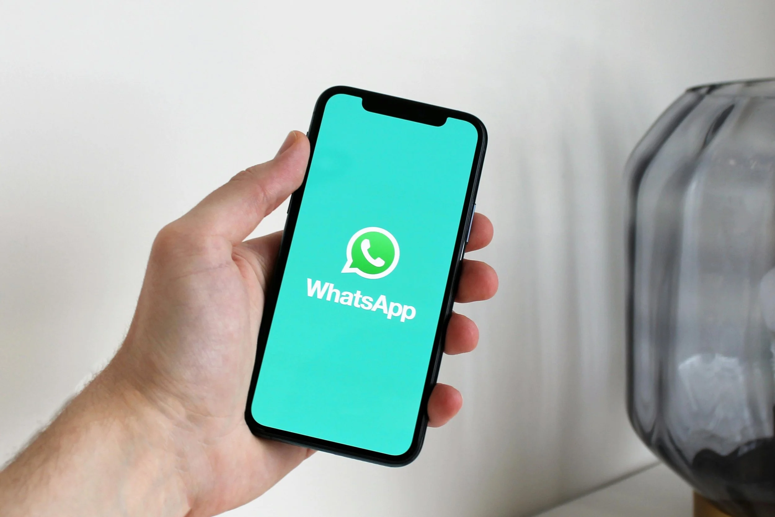A person holding a smartphone displaying the WhatsApp app logo on the screen.
