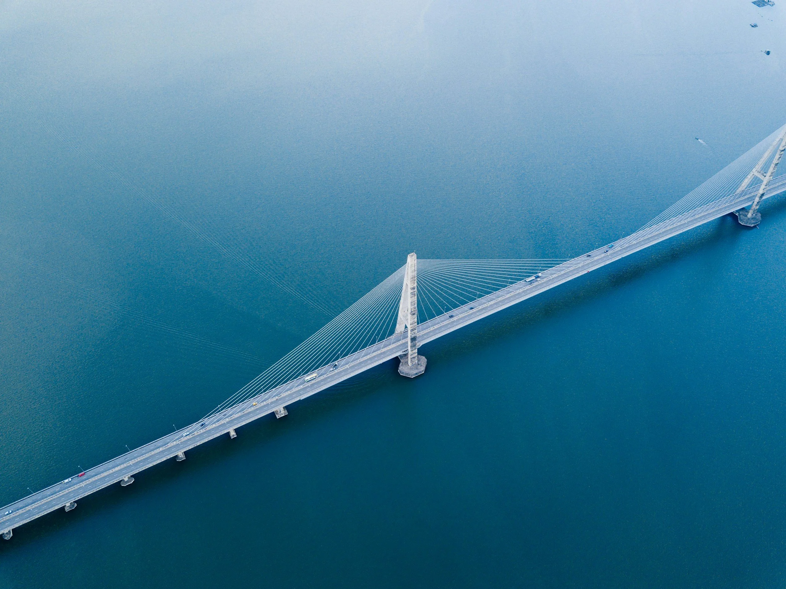 Aerial view of a modern suspension bridge over a body of water, with visible cables and two towers supporting the structure.