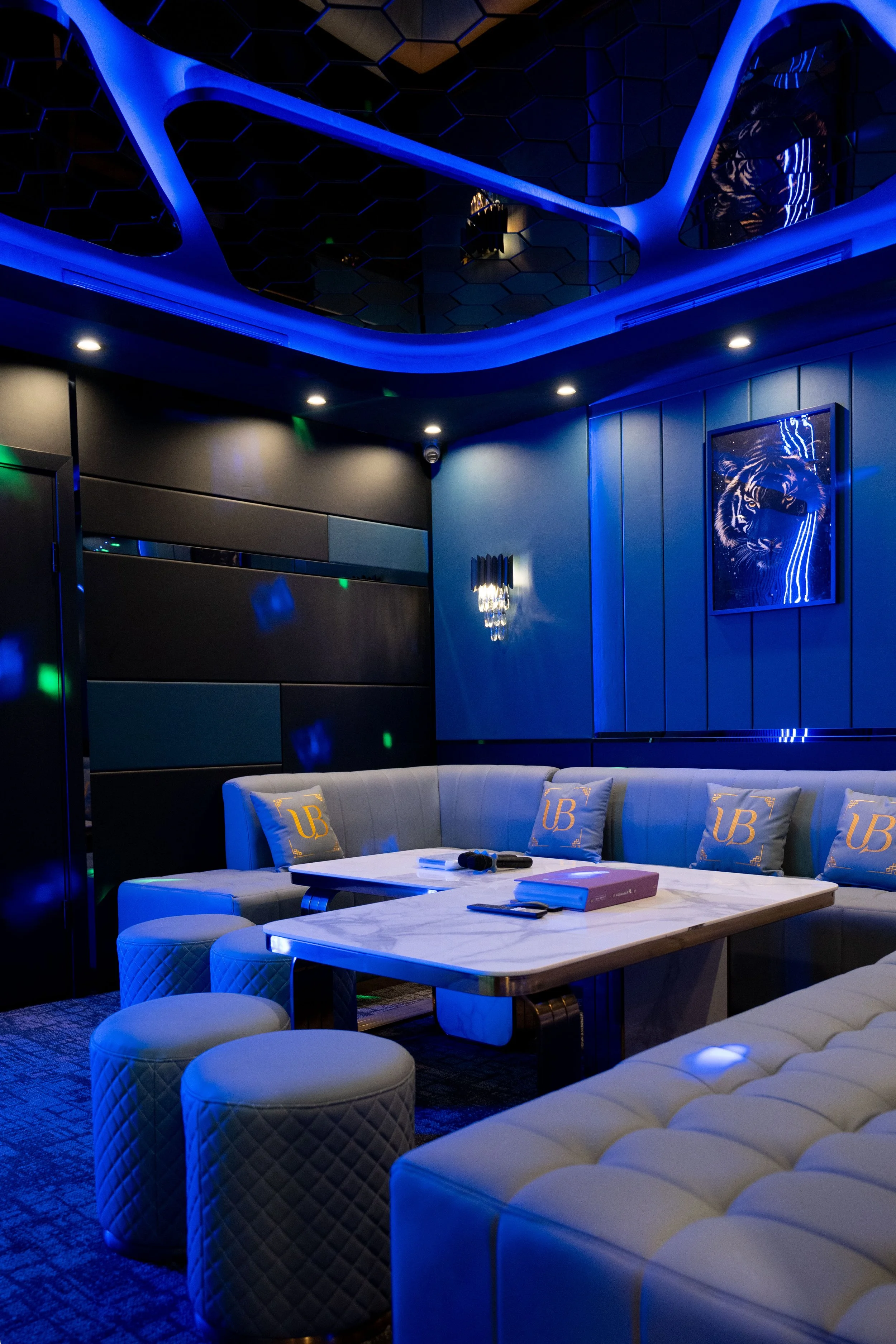 Inside a modern, luxurious lounge or private room with blue lighting, white leather seating, a marble table, and wall art featuring a tiger with neon-like blue accents.