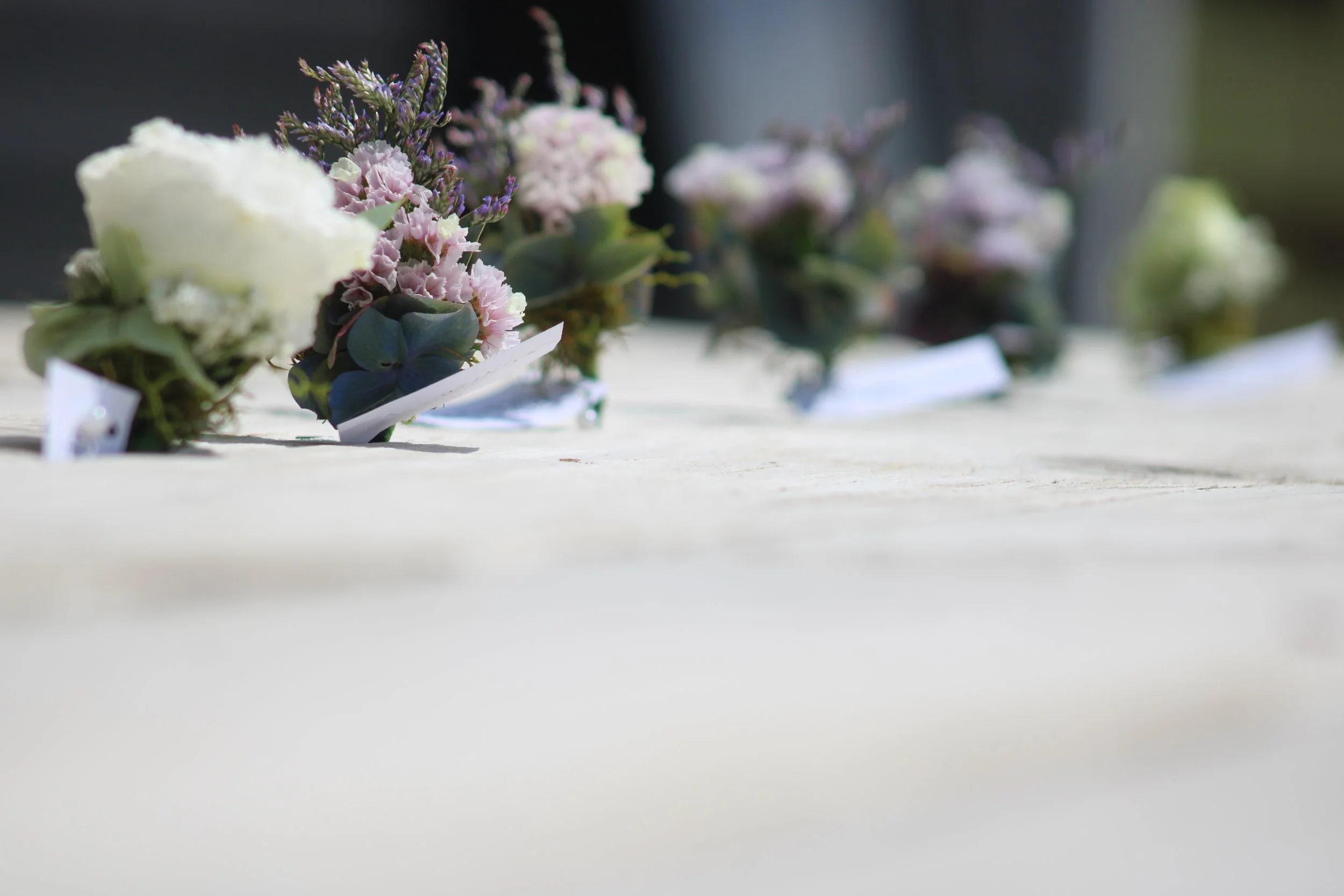 A row of small flower arrangements with various pink, purple, and white flowers on a white surface, out of focus in the background.
