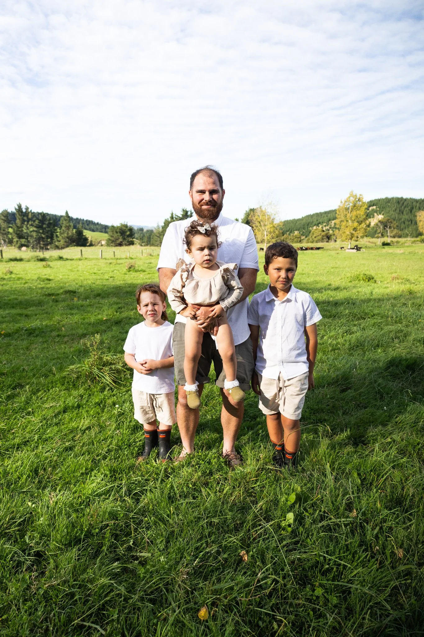 A man with three children standing in a green field with trees and hills in the background.