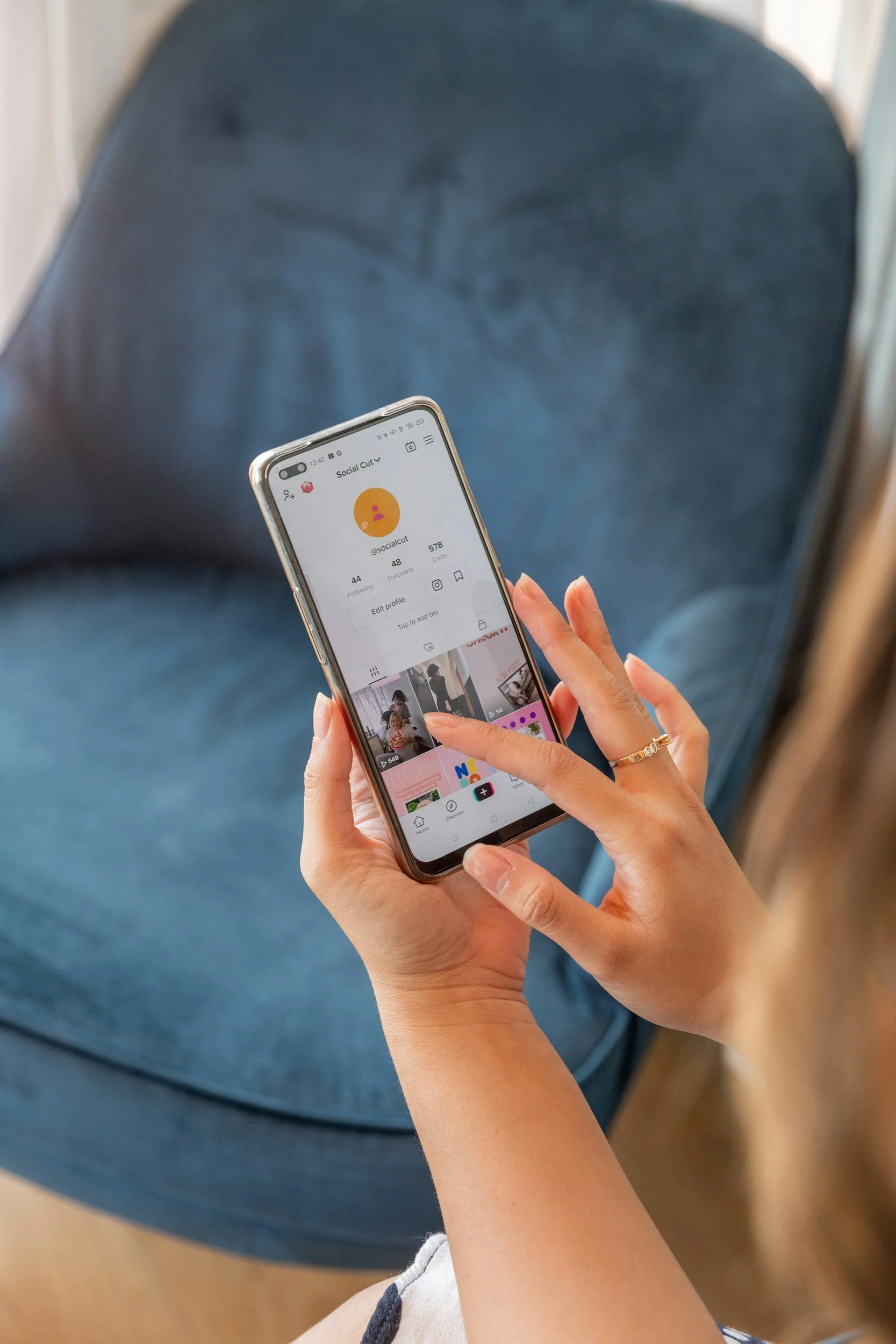 Person holding a smartphone showing a social media profile page indoors, with the focus on their hand and the phone screen.