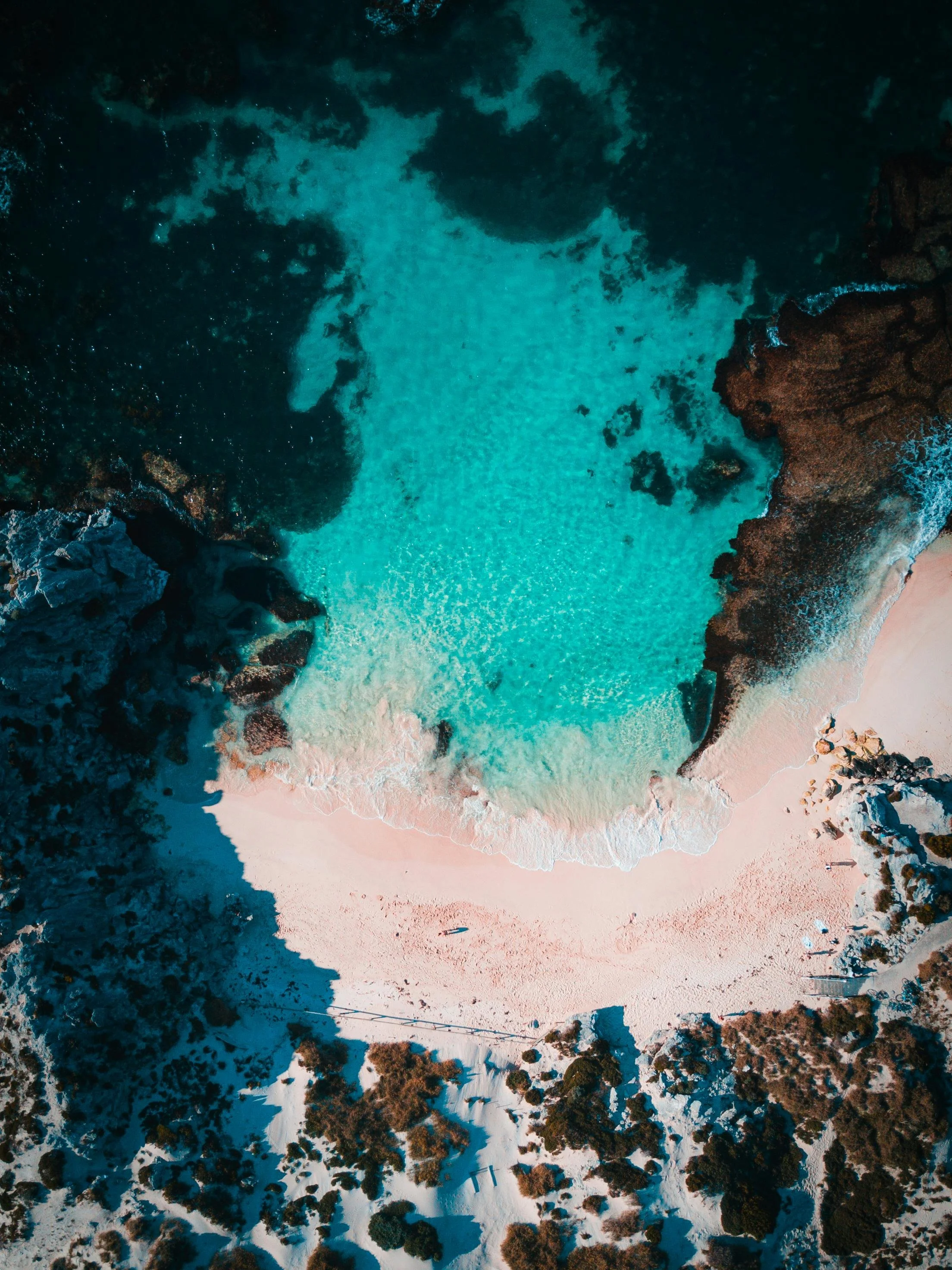 A bird's eye view of a cove with turquoise water surrounded by rocky cliffs and a sandy beach.