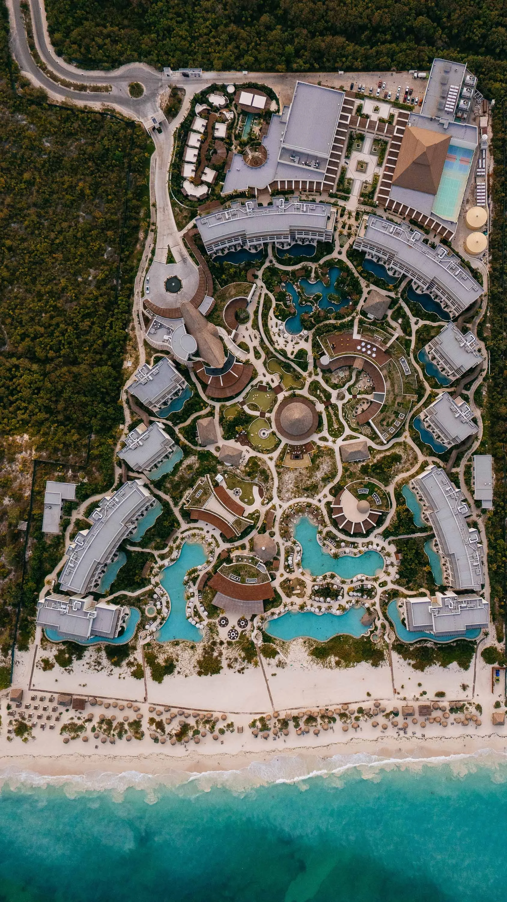 An aerial view of a large beachfront resort with multiple pools, buildings, and lush landscaping.
