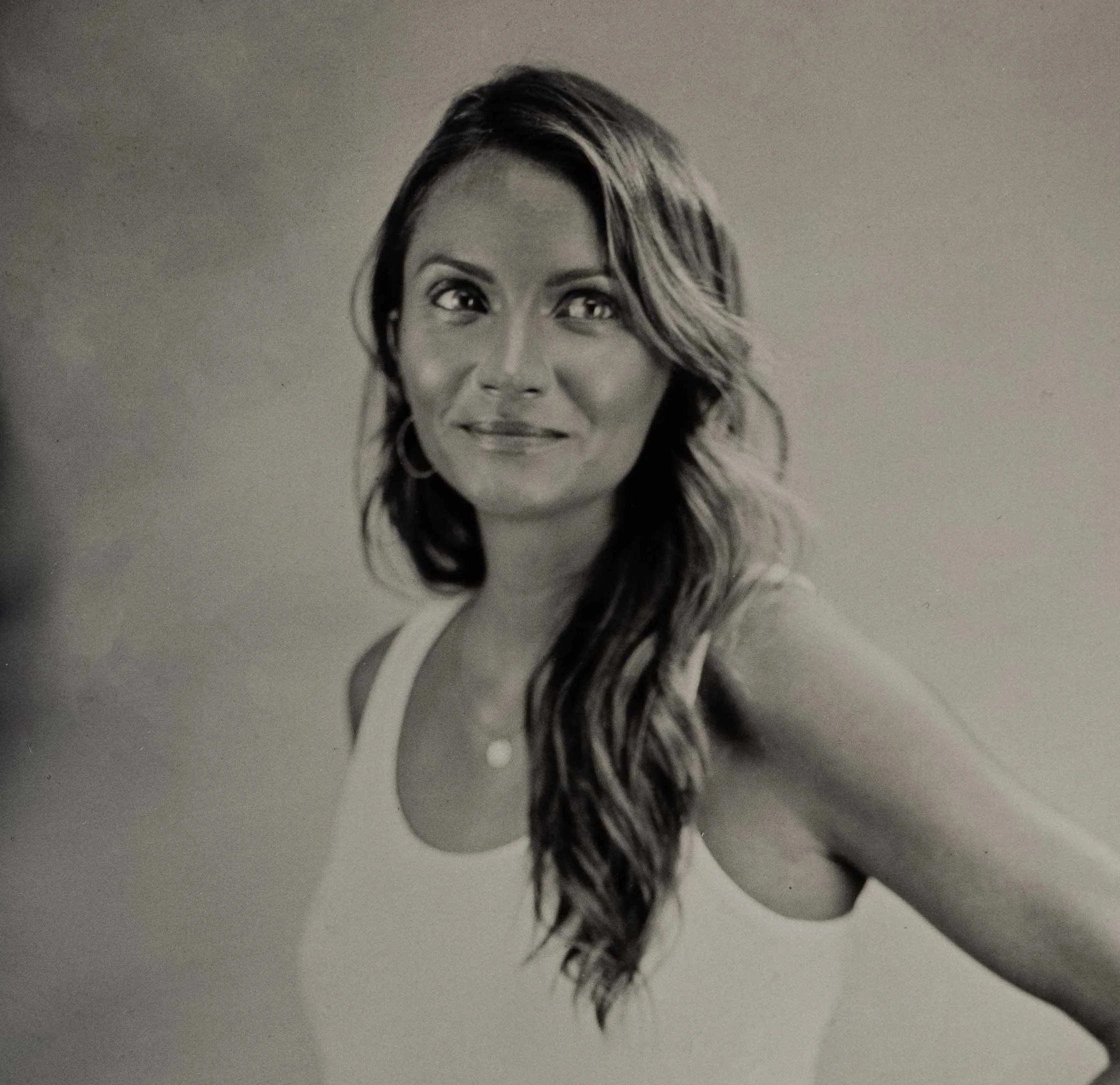 Black and white portrait of a smiling woman with long wavy hair wearing a sleeveless top.