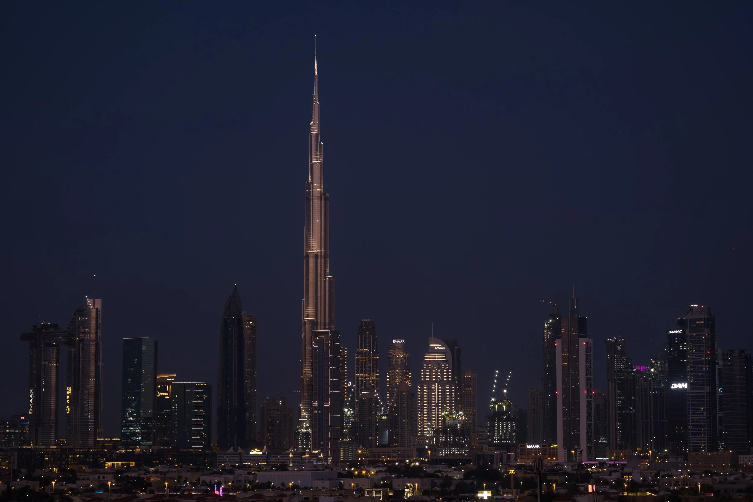 Nighttime view of Dubai skyline featuring the Burj Khalifa, the tallest building, with illuminated skyscrapers surrounding it.