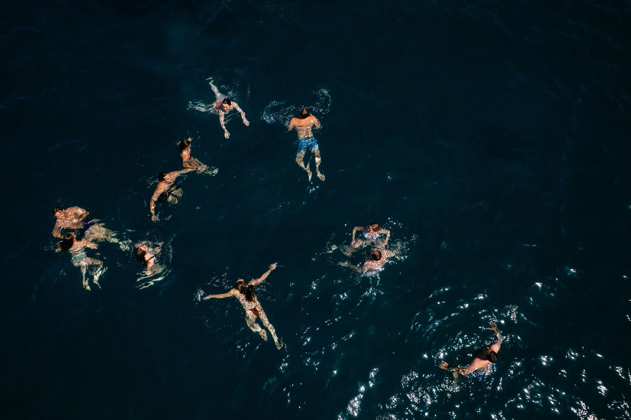 People swimming in a dark blue ocean from an aerial view.