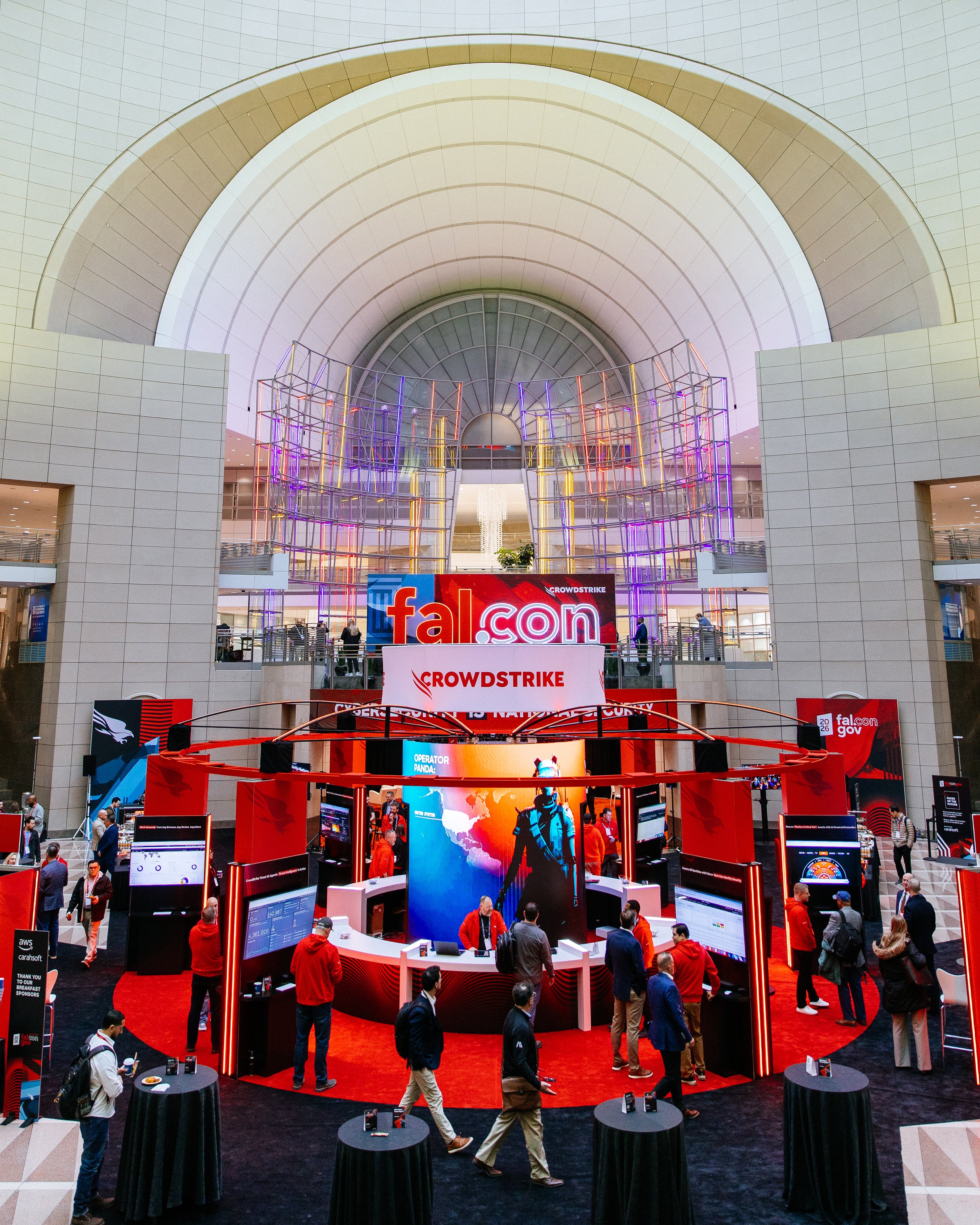 People attending a Falcon-themed event at a conference center with a large digital display, colorful lighting, and a promotional setup.