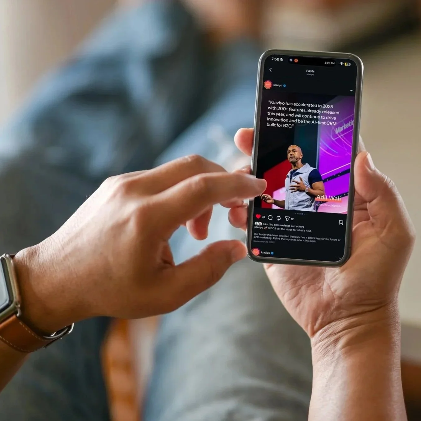 Person holding a smartphone displaying a social media post about Klaviyo, with a picture of a man giving a presentation against a purple and pink background.