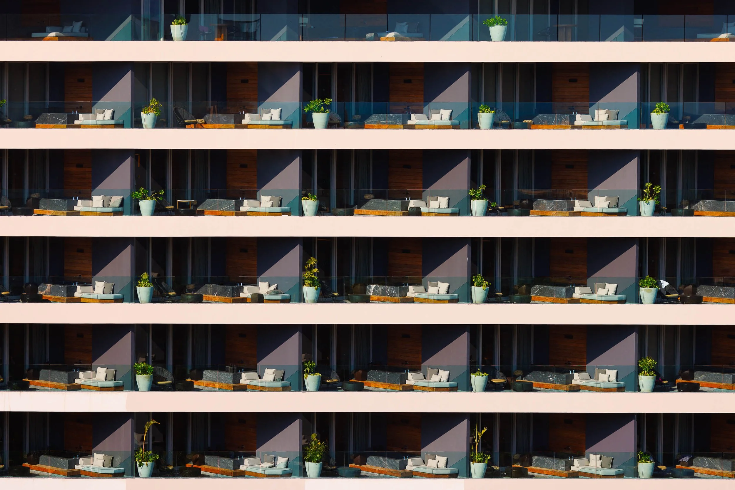 Multiple hotel balcony patios featuring chairs, tables, potted plants, and glass barriers, arranged in a grid pattern across several floors of the building.