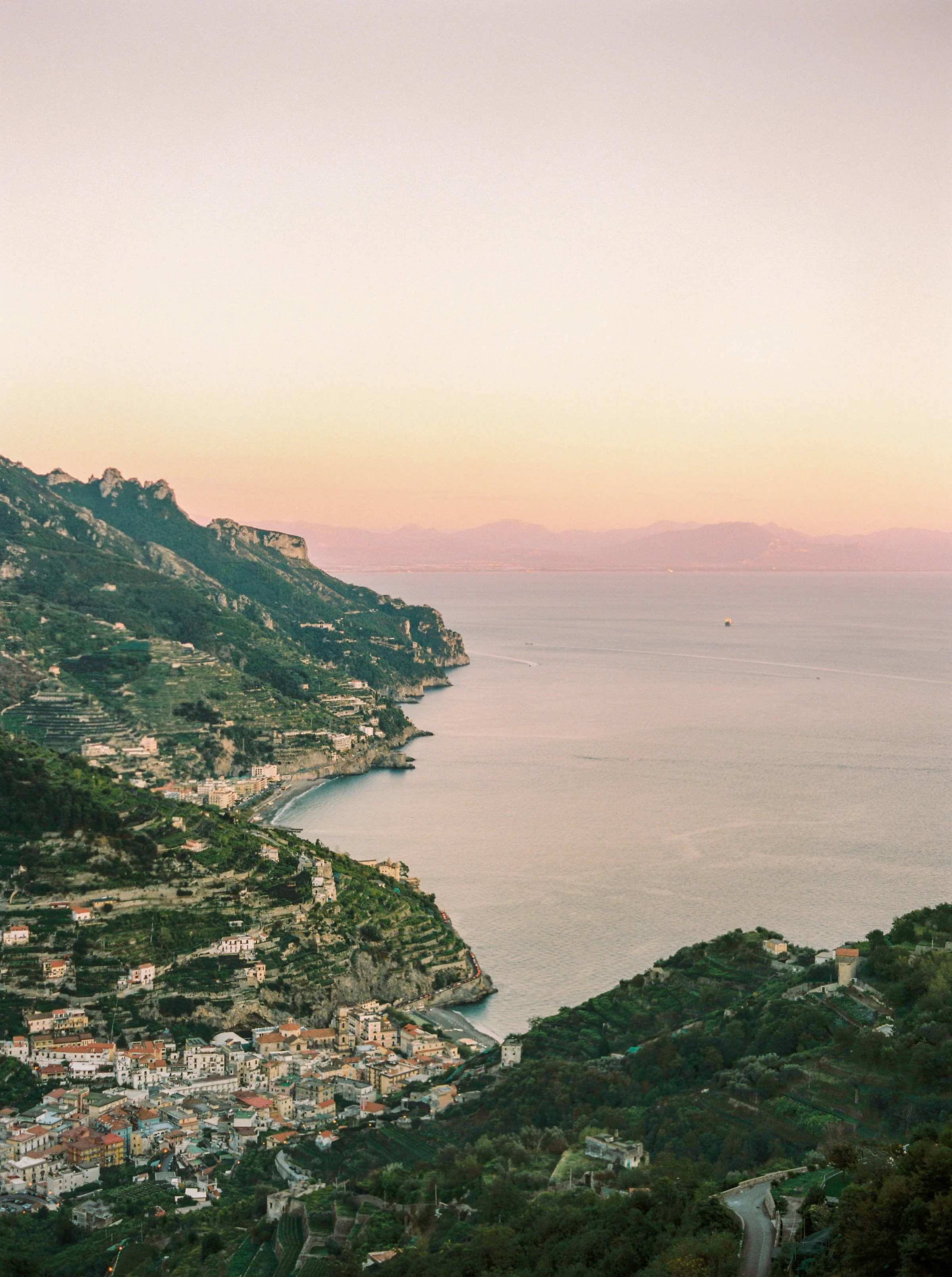 Scenic view of a coastal town with terraced vineyards and houses on hillside, overlooking the sea at sunset. Scenic coastal view at women's retreat destination Mallorca Spain
