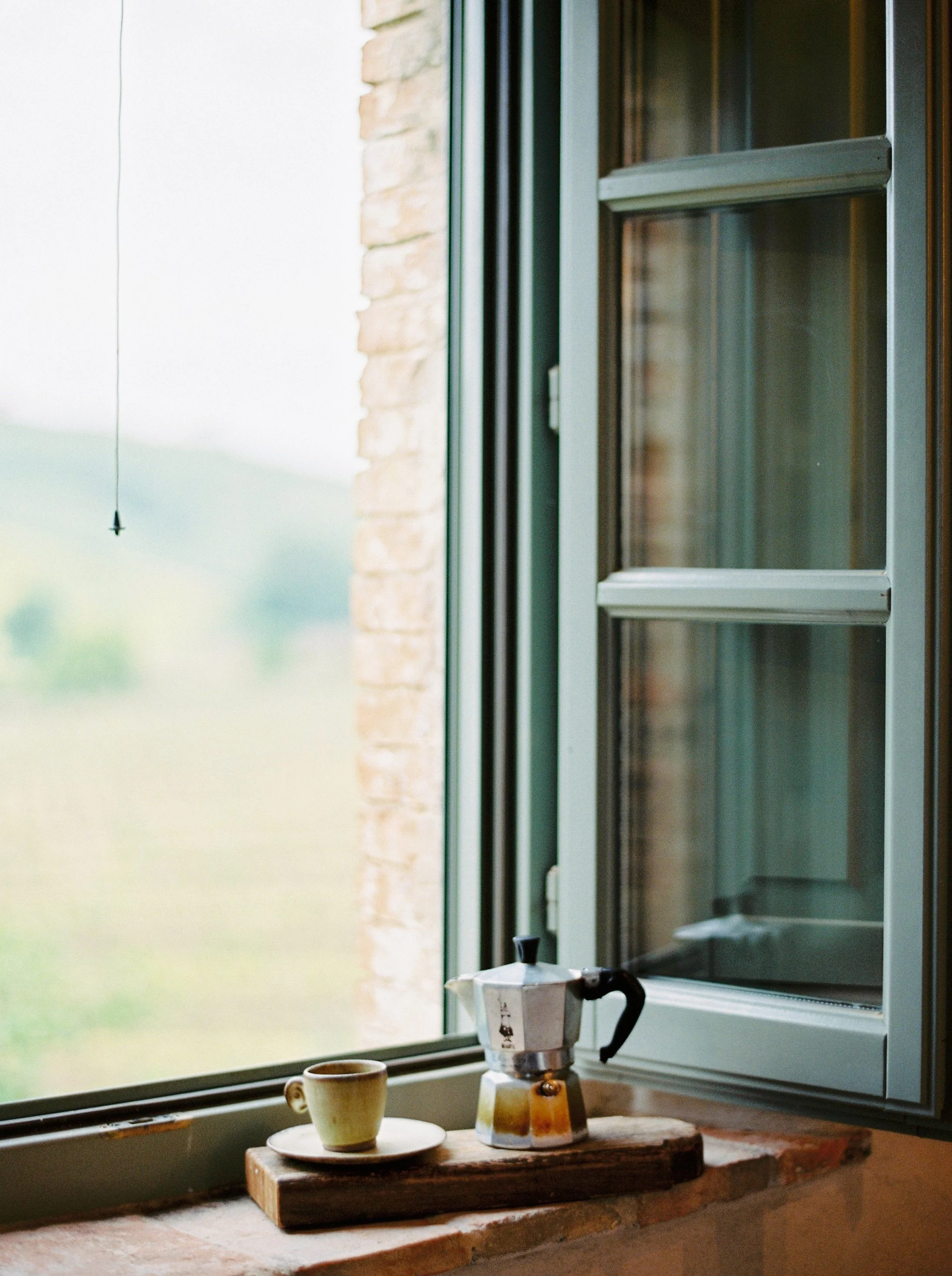 Kitchen window overlooking the Umbrian countryside with a moka pot and cup — a quiet moment from a women’s retreat in Italy.