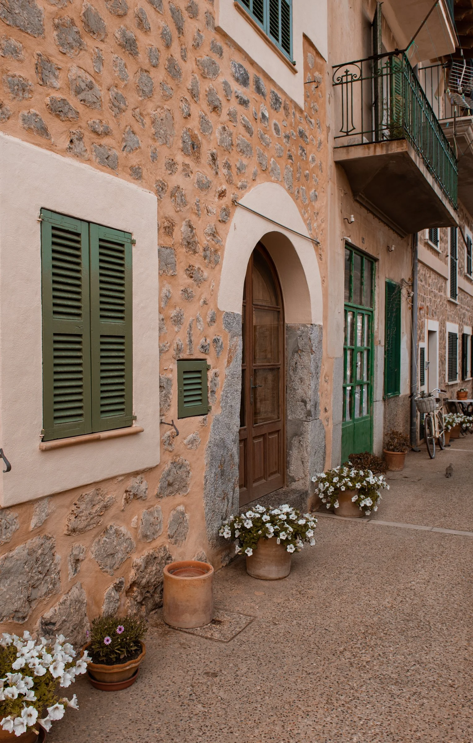 Rustic stone building with green shutters and a bicycle outside, a European street scene from a women’s travel retreat destination.