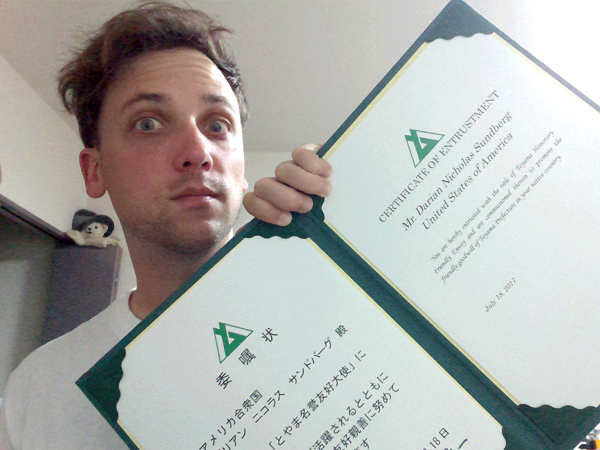 A man holding two certificates, one in English and one in Japanese, with a surprised expression.