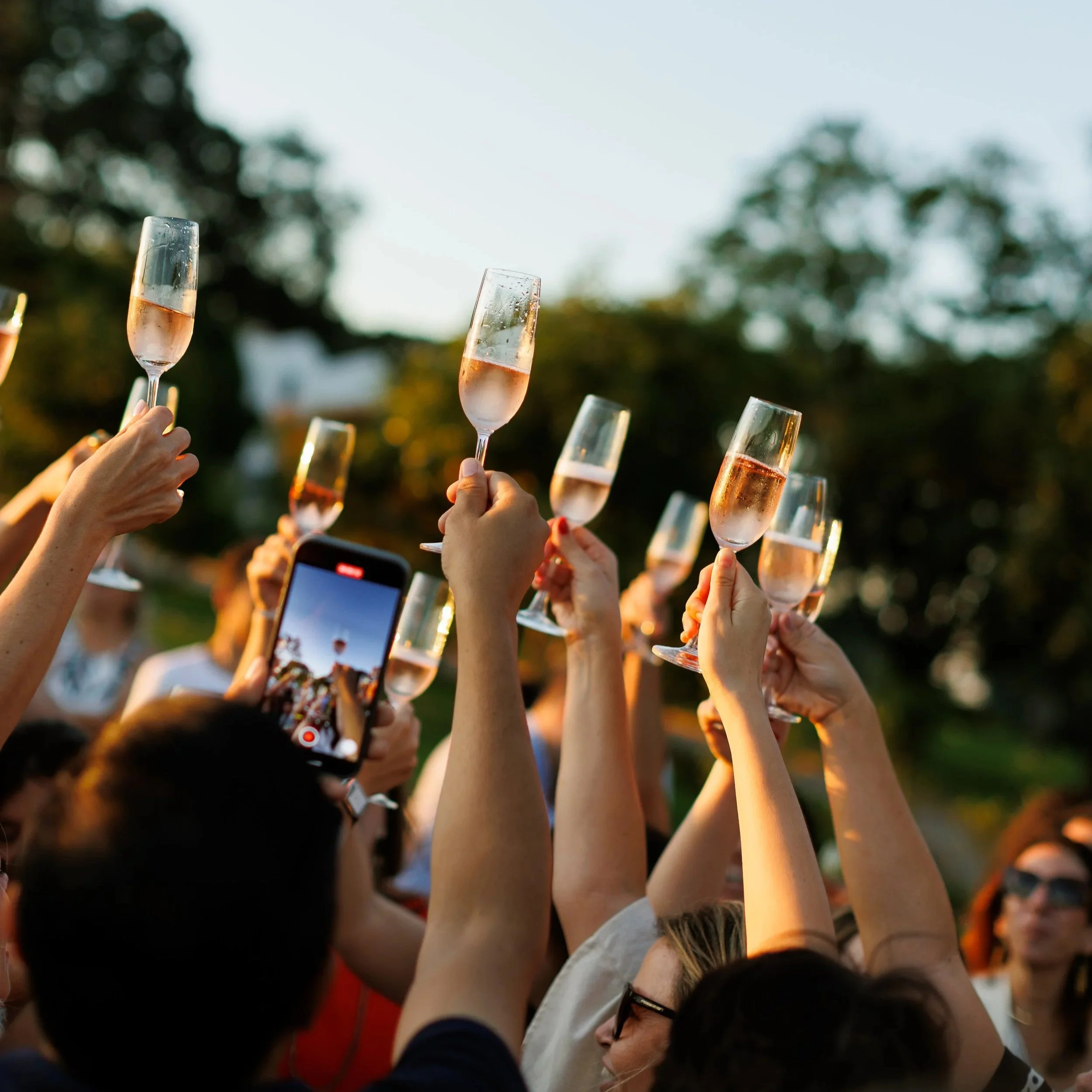 Pessoas levantando taças de espumante em celebração ao ar livre ao entardecer.