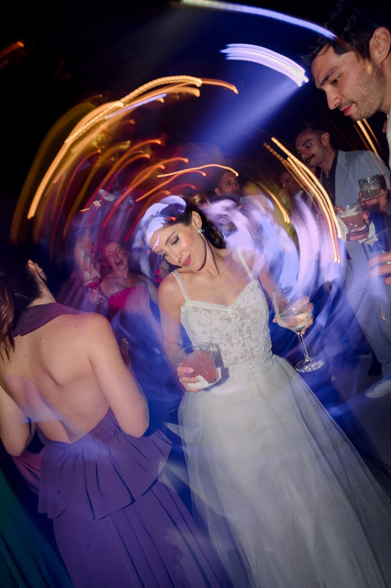 Mulher dançando em festa, usando vestido branco e segurando copo.