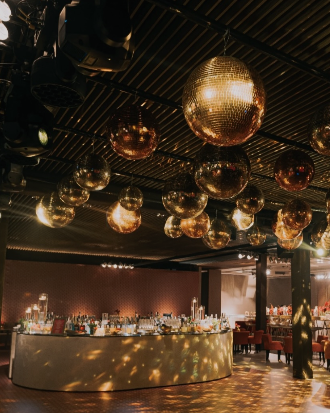Decoração de festa com bolas de espelho penduradas no teto, iluminação suave, balcão com comidas e bebidas, cadeiras industriais em um ambiente interno sofisticado.