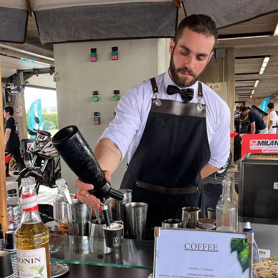 Barista preparando café em uma bancada com diversas bebidas e utensílios.