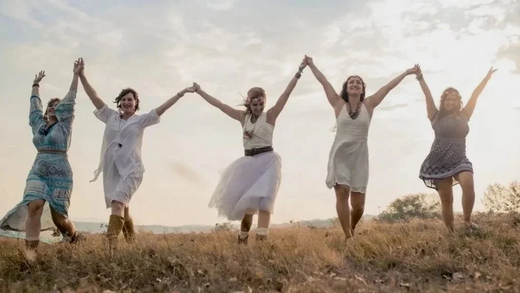 Happy women holding hands with arms raised in a field of grass.