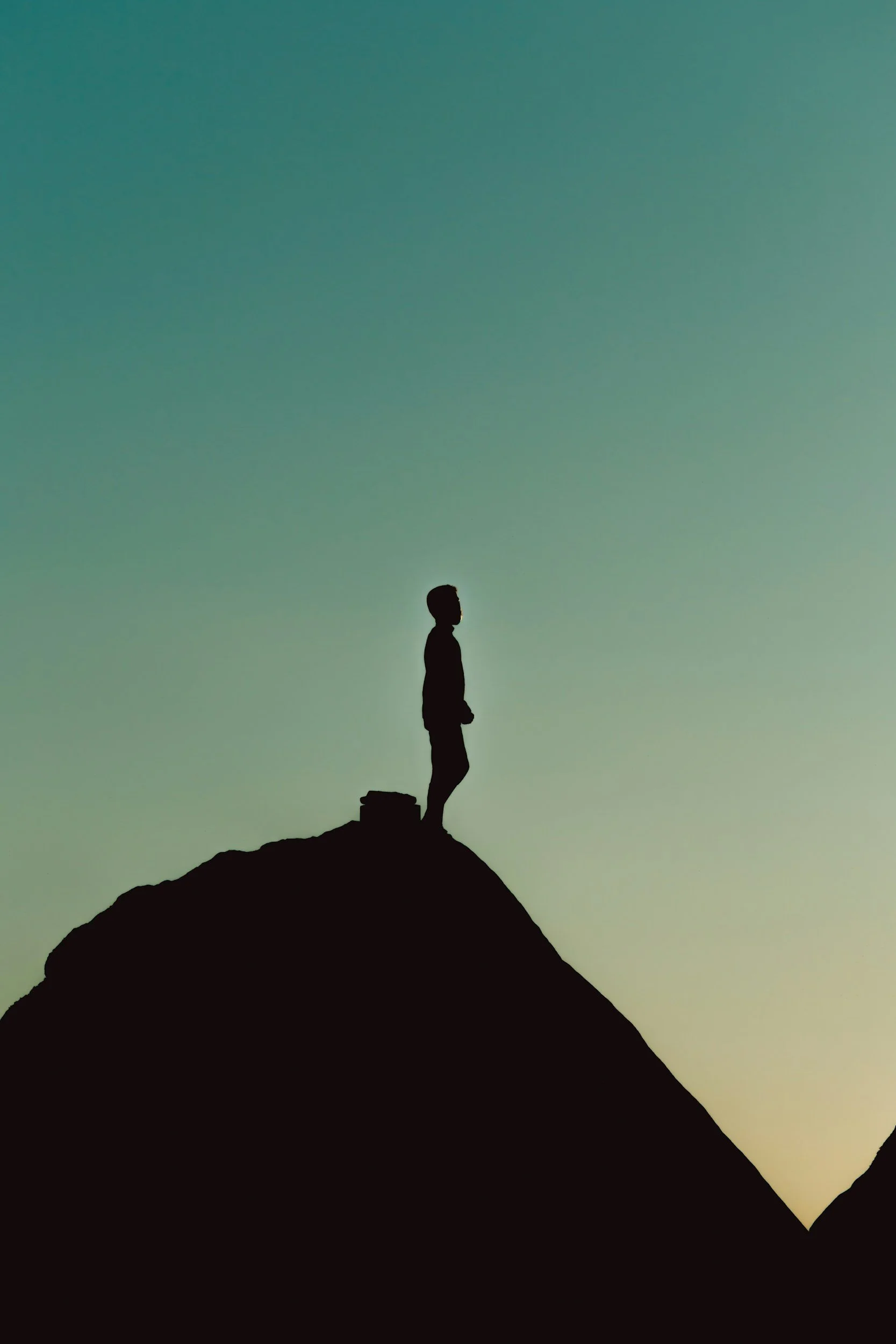 Silhouette of a person standing on a mountain peak against a gradient sky at dusk.