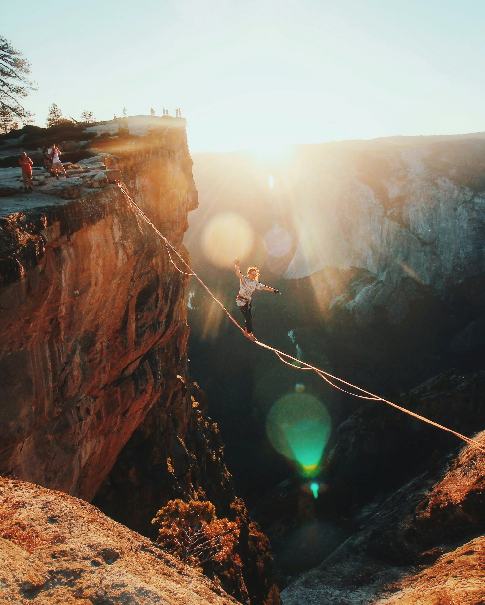 Hikers and a person walking on a mountain cliff with sunlight shining and lens flare effects in a rugged canyon landscape.