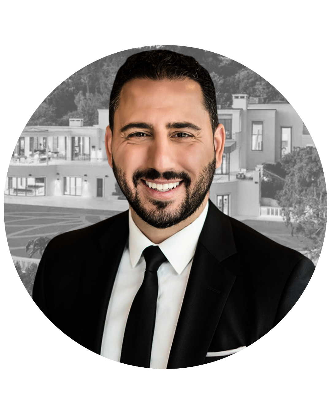 A smiling man with dark hair and a beard in a black suit, white shirt, and black tie, in front of a modern residential building.