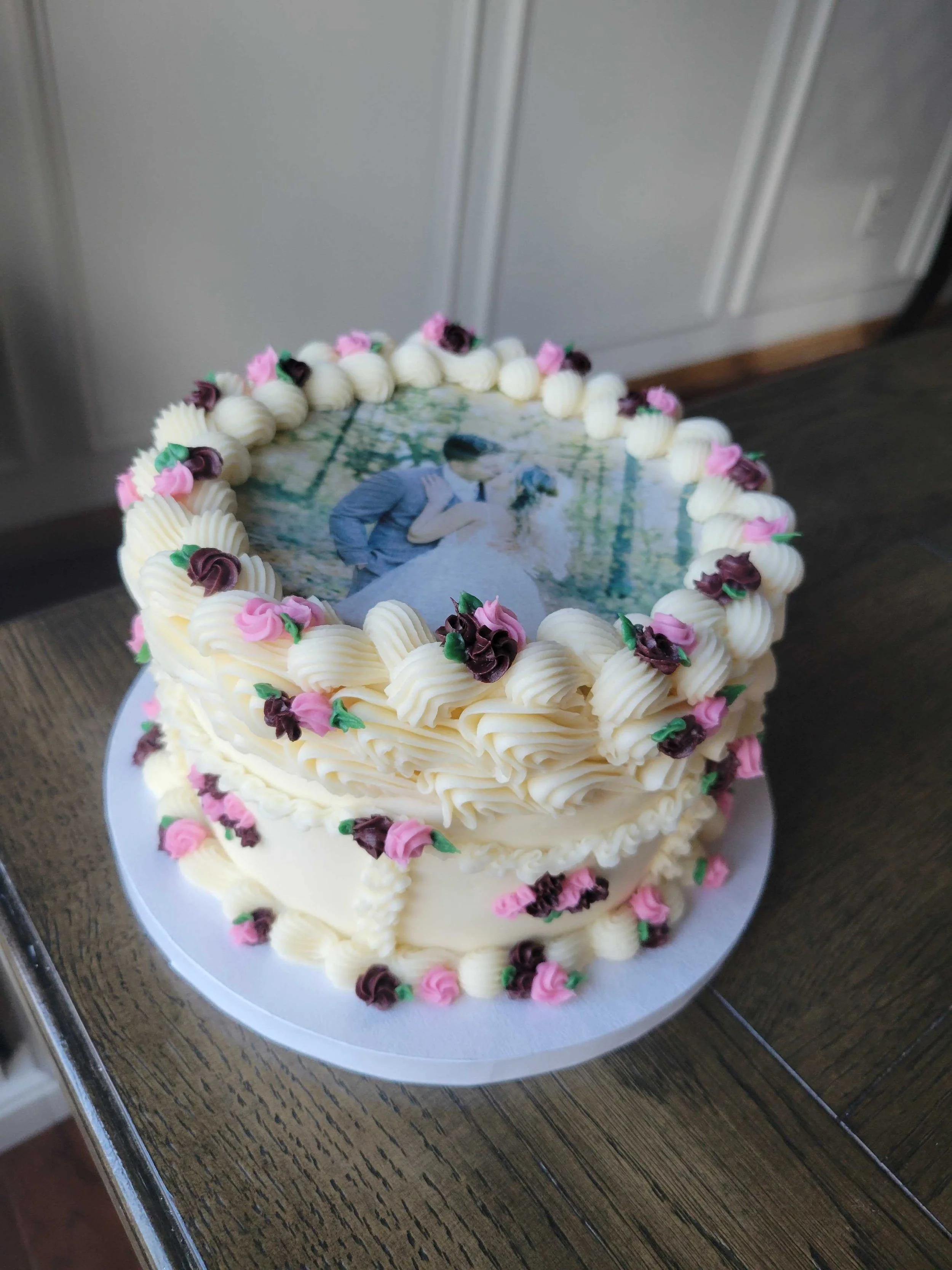 A wedding cake with a printed edible photo of a bride and groom on the top, decorated with pink and purple frosting flowers and cream-colored piping.