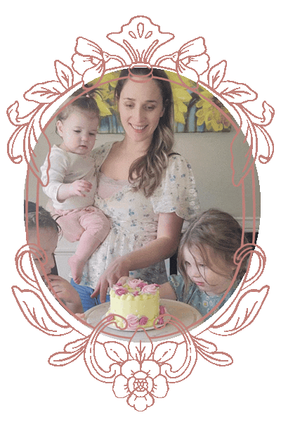 A woman with two young children celebrating a birthday with a cake on a table, with a pink decorative frame around the image.