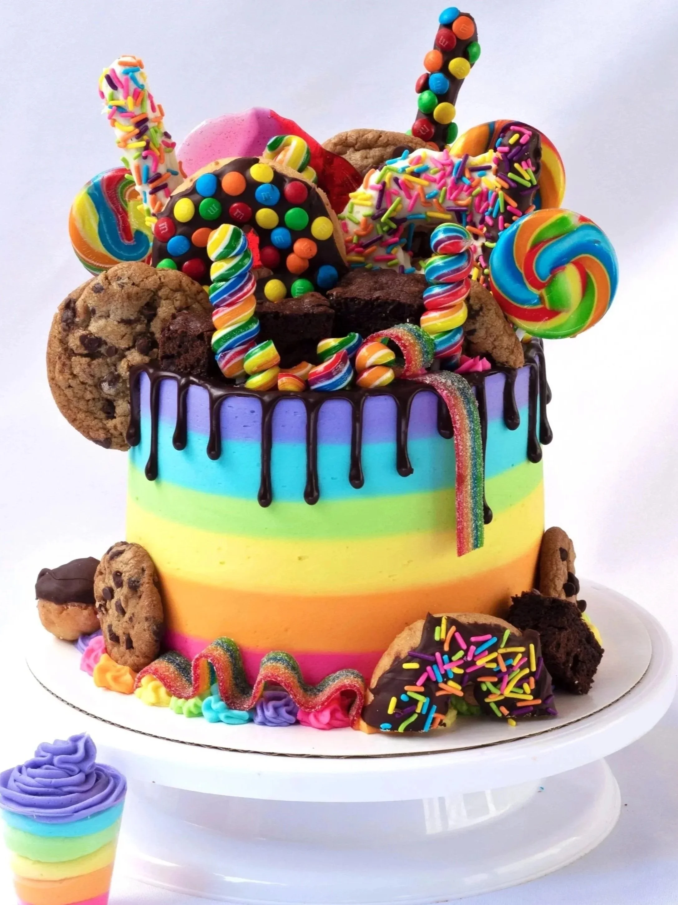 Colorful rainbow cake topped with various candies, cookies, and sprinkles.