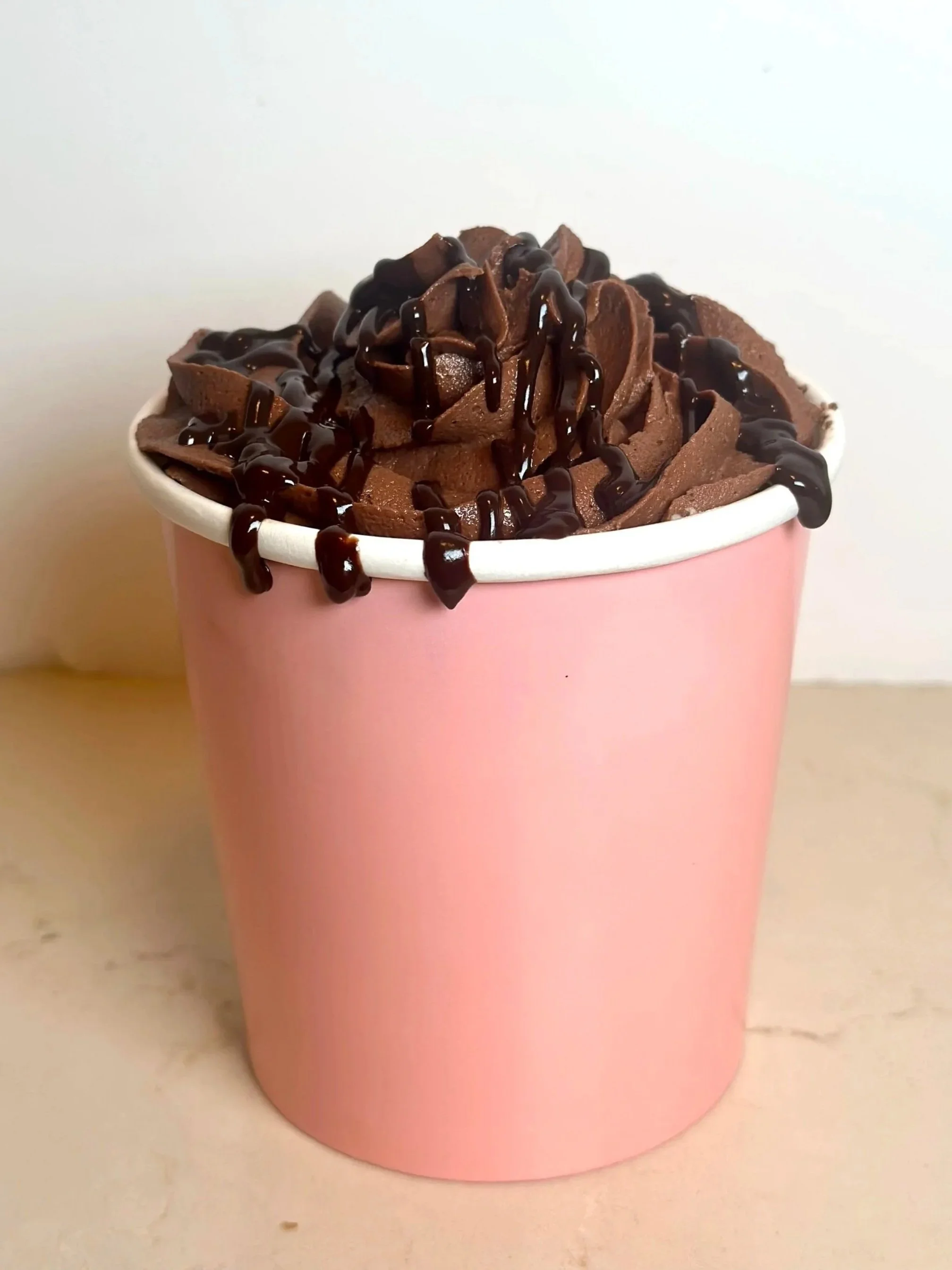 Pink cup filled with chocolate ice cream topped with chocolate syrup.