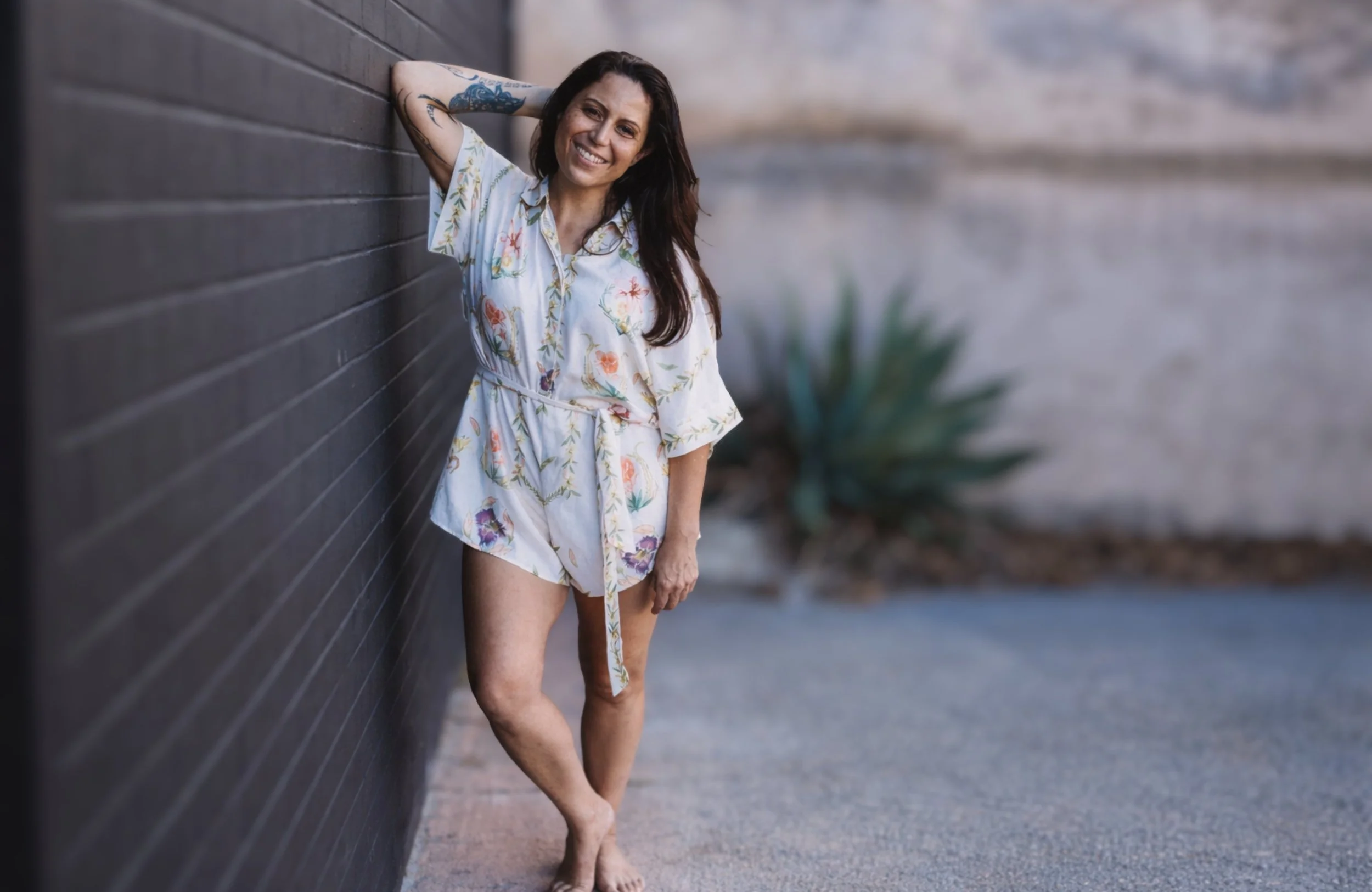 Natalie Seigne smiling and leaning against a wall, capturing a warm, grounded presence. Reflecting her work in intuitive guidance, energy healing and supporting others to feel safe, seen and gently guided toward clarity and direction.