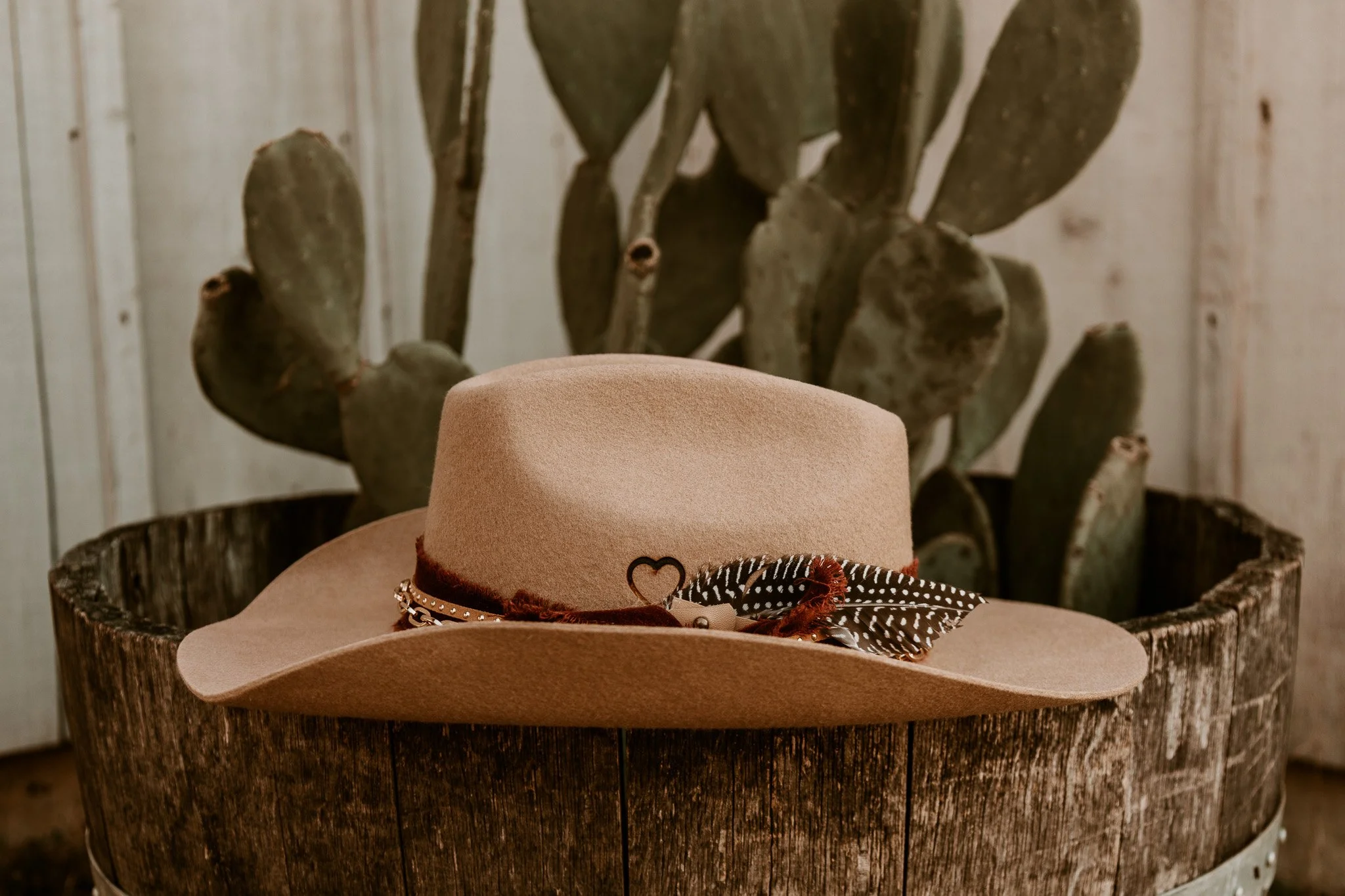A beige wide-brimmed hat with a decorative band and bow resting on a rustic wooden container, with a cactus plant in the background.