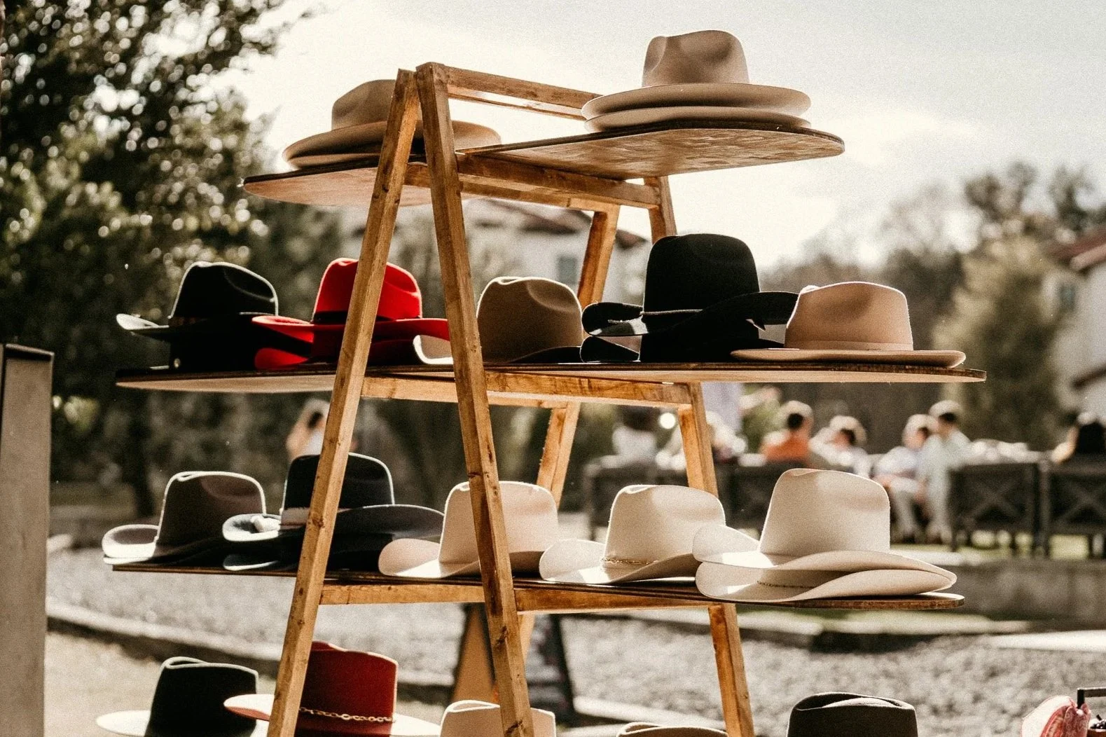 Display of cowboy hats in various colors on wooden shelves at an outdoor market.
