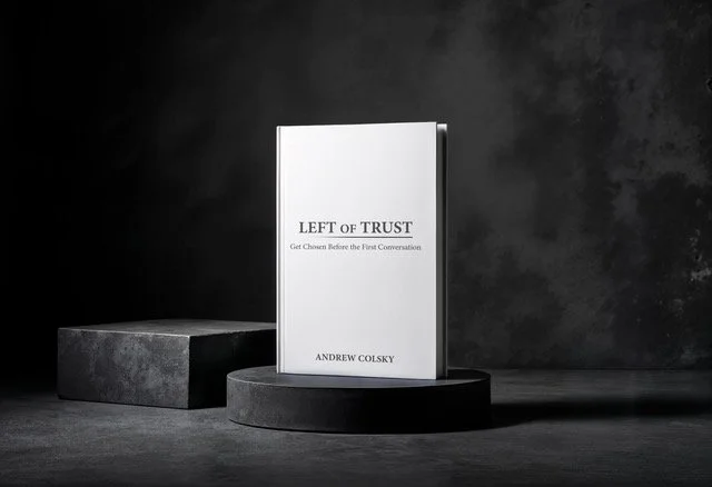 A book titled 'Left of Trust' by Andrew Colsky displayed on a round black pedestal, with a concrete block beside it, against a dark textured background.