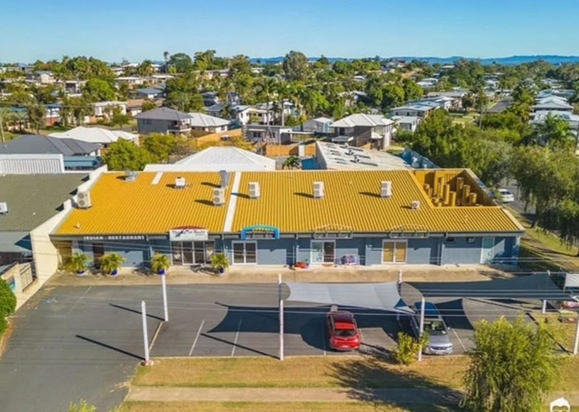 Aerial view of a commercial building with a bright yellow roof and parking lot in front, located in a suburban area with houses and trees around.