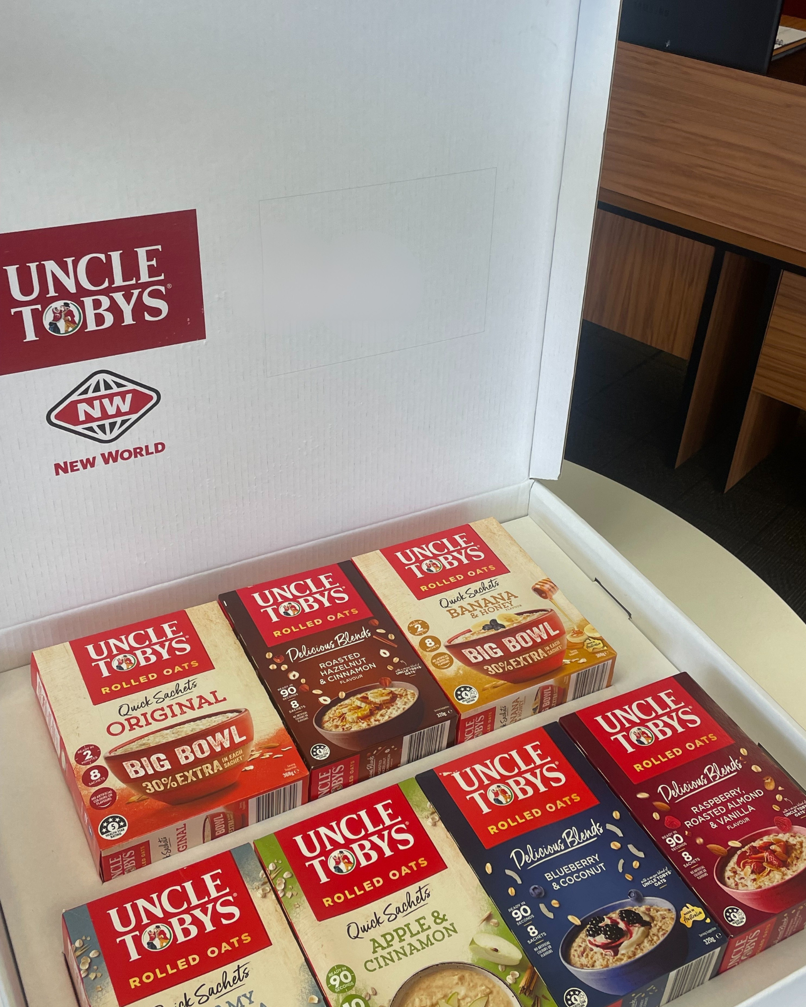 Boxes of Uncle Tobys rolled oats, including Original, Roasted Hazelnut & Cinnamon, Banana & Honey, Apple & Cinnamon, and Blueberry & Coconut flavors, displayed on a white counter.