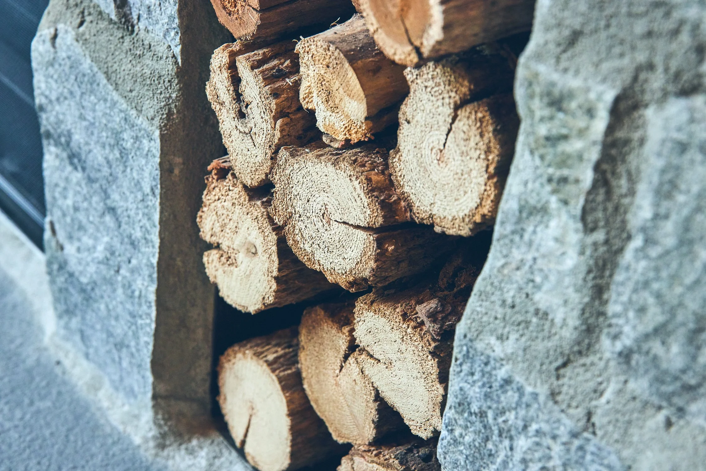 Close-up of stacked firewood pieces against a stone surface.