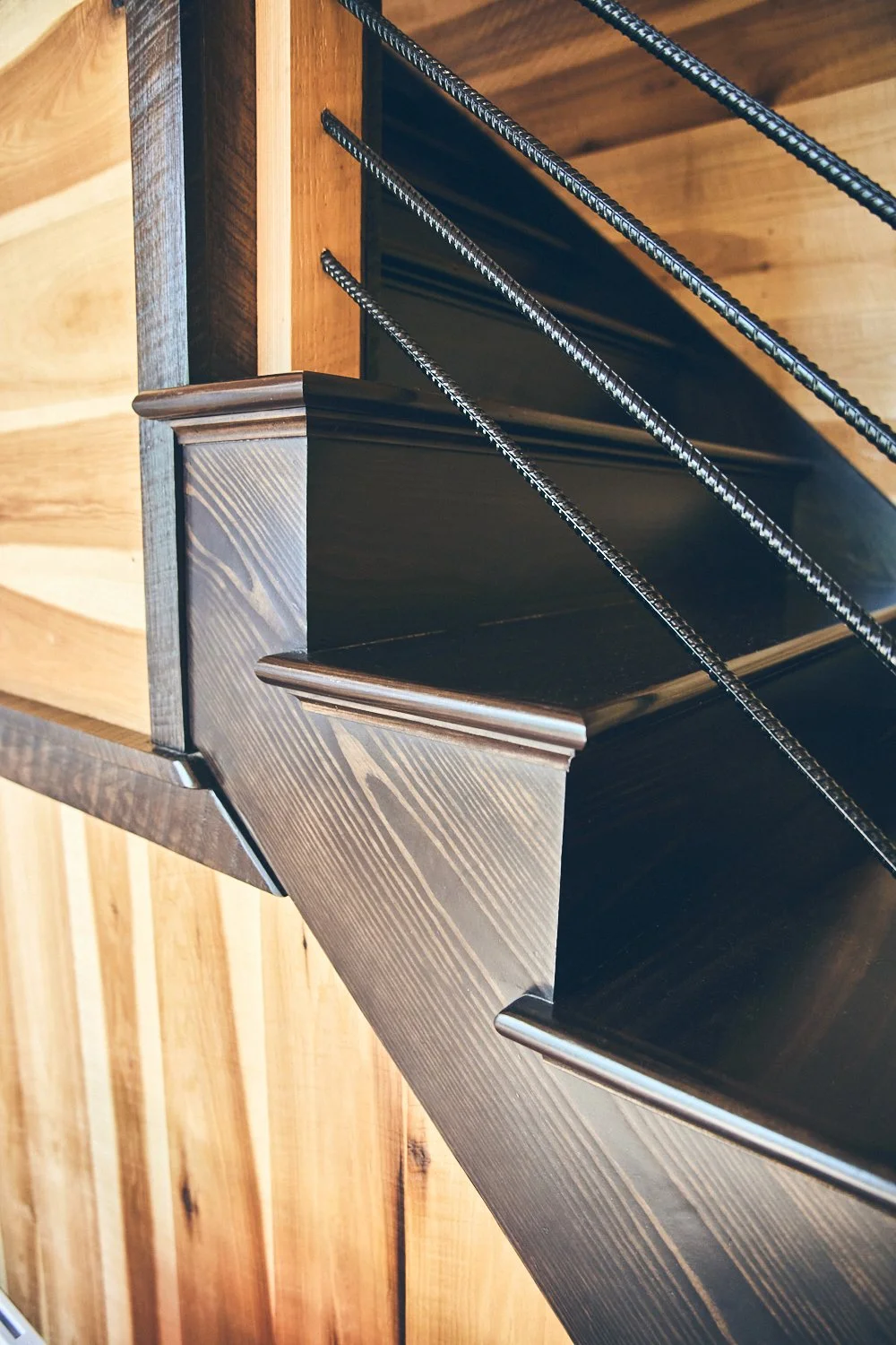 Close-up view of a wooden stair railing with dark metal balusters against a background of wooden paneling.