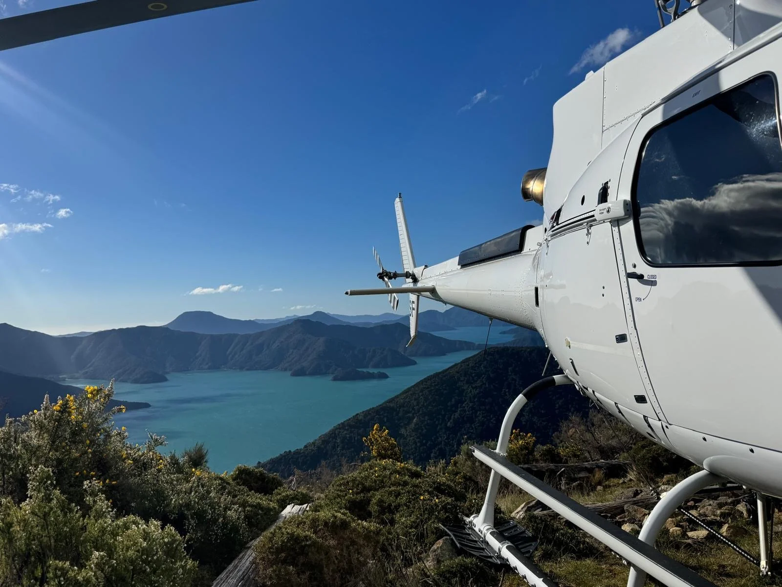 A helicopter flying over a scenic landscape of mountains and a lake, with clear blue skies
