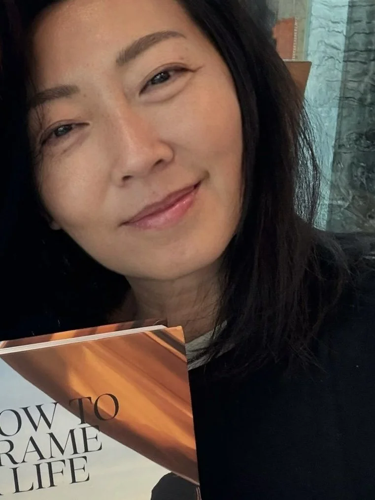 Close-up of a woman smiling, holding a book titled "How to Reframe Your Life".