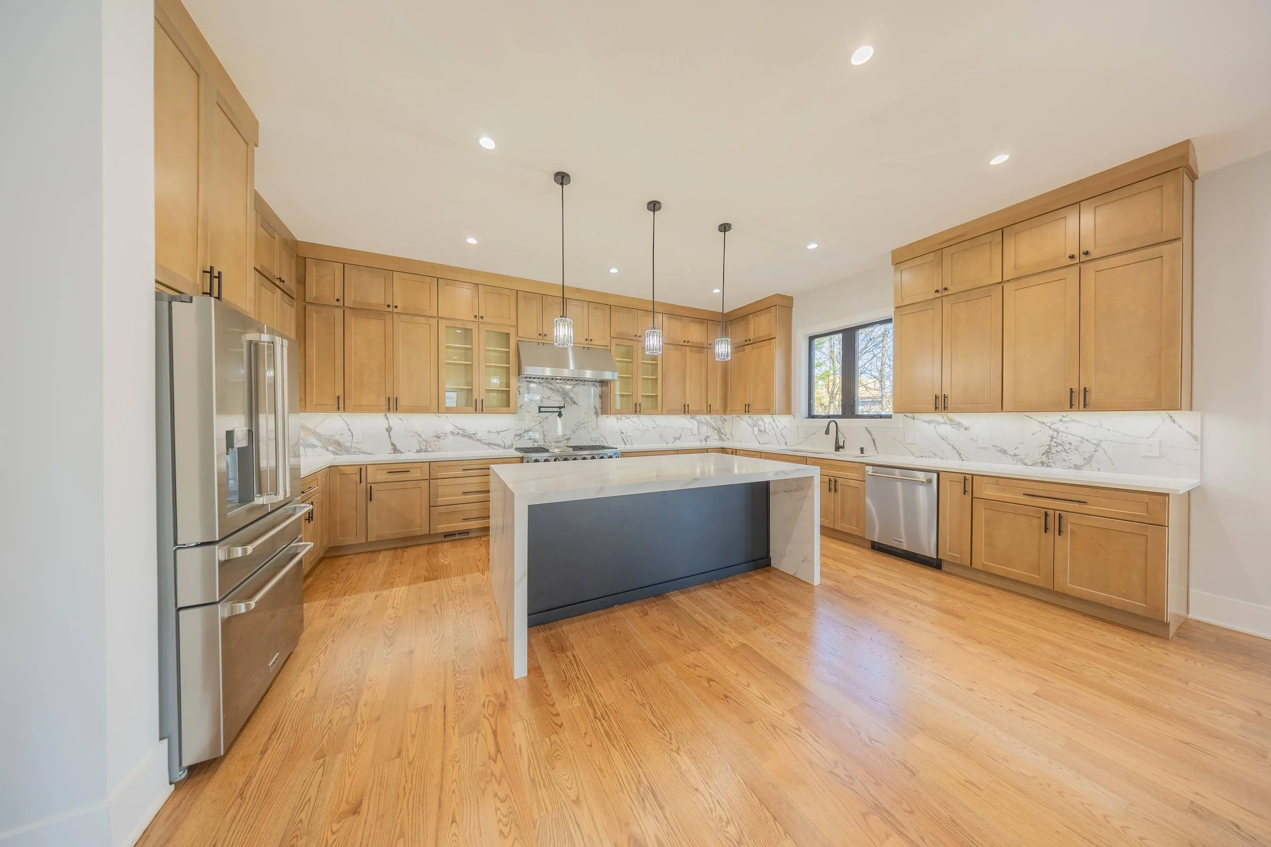A kitchen with wooden floor and cabinets, and marble table and backsplash