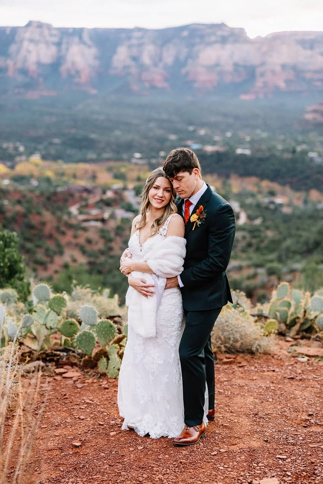 Newlywed couple standing on a red-soil desert trail lined with cacti during their Sedona elopement, mountains in the distance