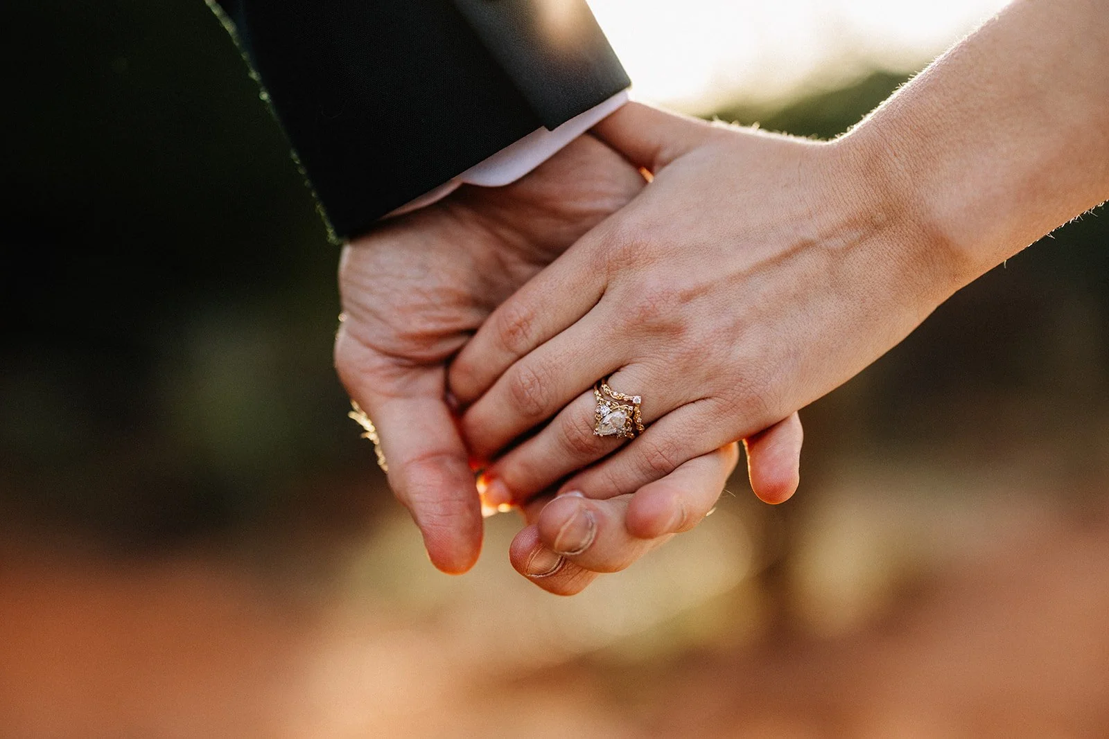 Close-up of a couple's hands holding each other, with both wearing rings, during a wedding or engagement ceremony.